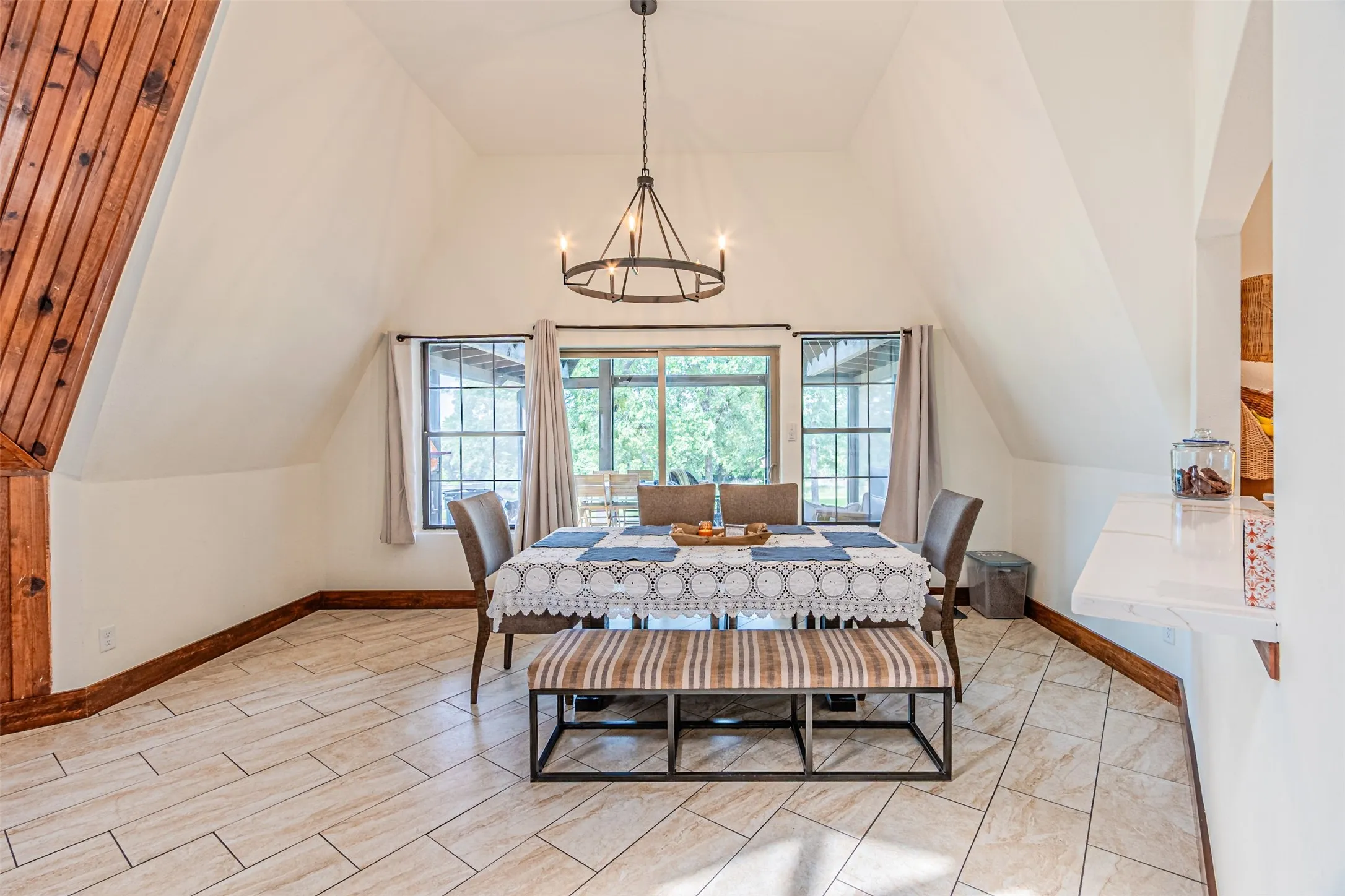 Vaulted ceiling dining area featuring wood-finish flooring, a contemporary chandelier, multiple windows, and a built-in breakfast bar