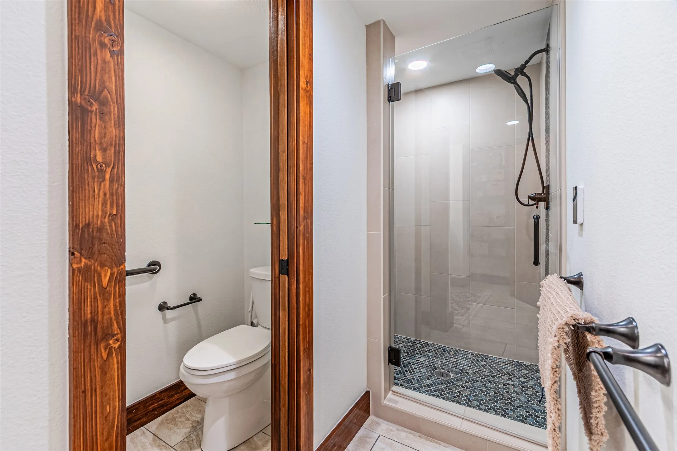 Glass-enclosed shower with pebble-tile flooring and matte bronze fixtures
