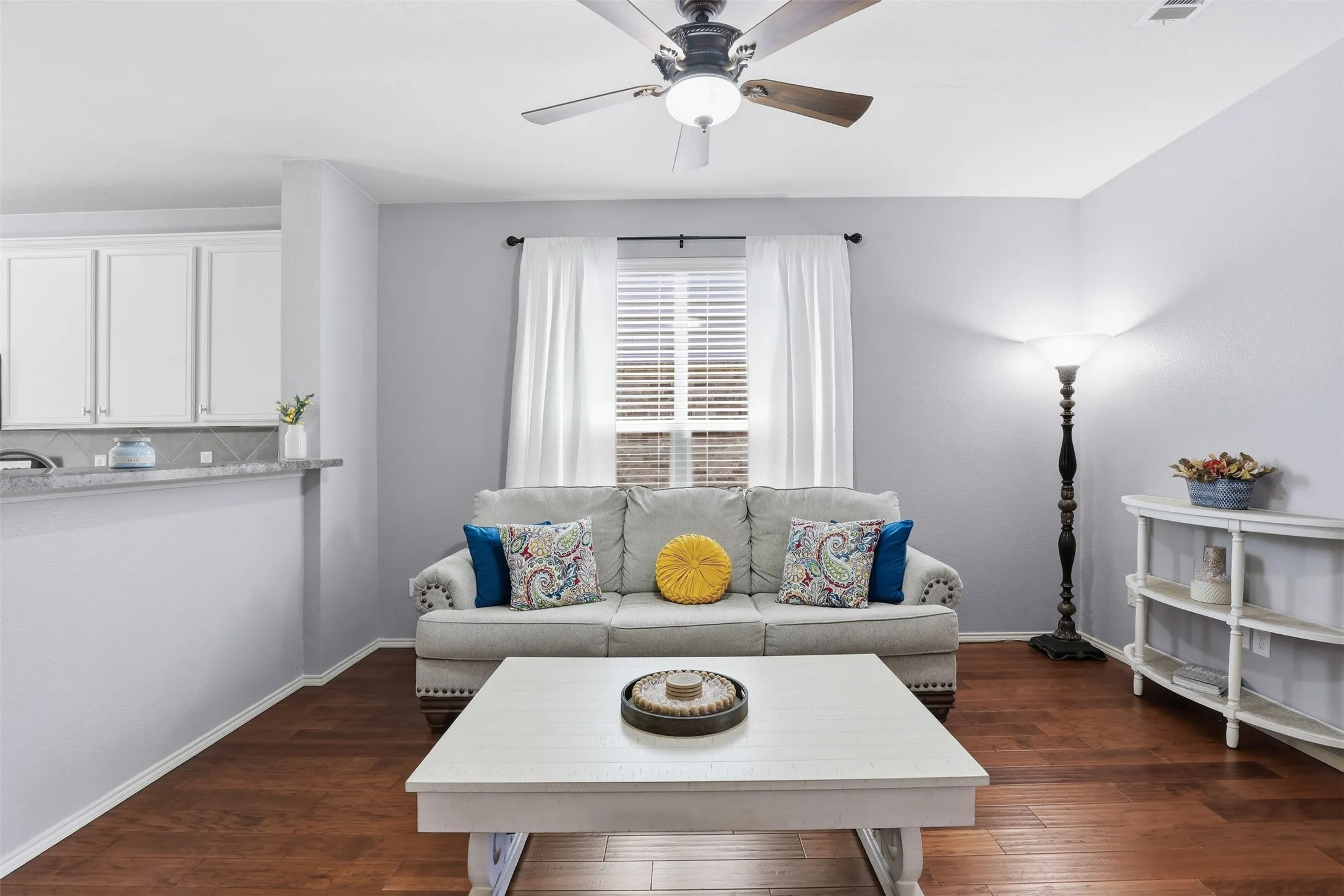 Living area featuring wood-finish flooring, a ceiling fan with integrated lighting, and a window with blinds and white drapes