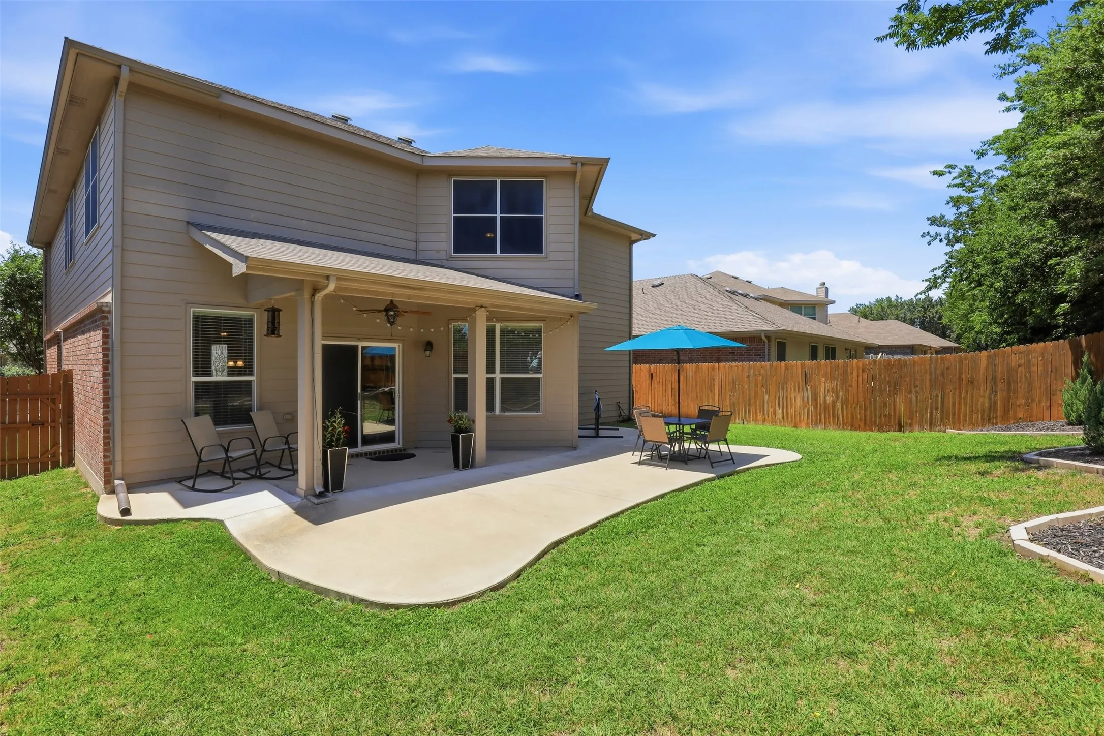 Expansive backyard featuring a covered patio, concrete patio extension, full privacy fencing, and a manicured lawn