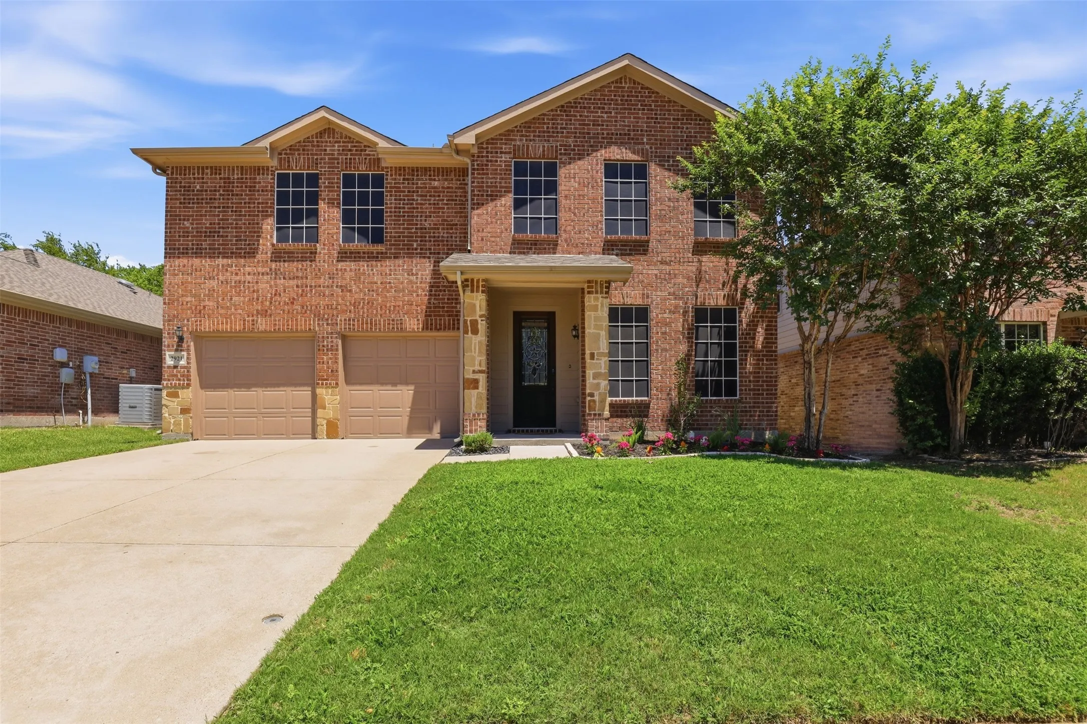 Two-story brick exterior featuring a covered entry, multiple windows, an attached two-car garage, and a concrete driveway