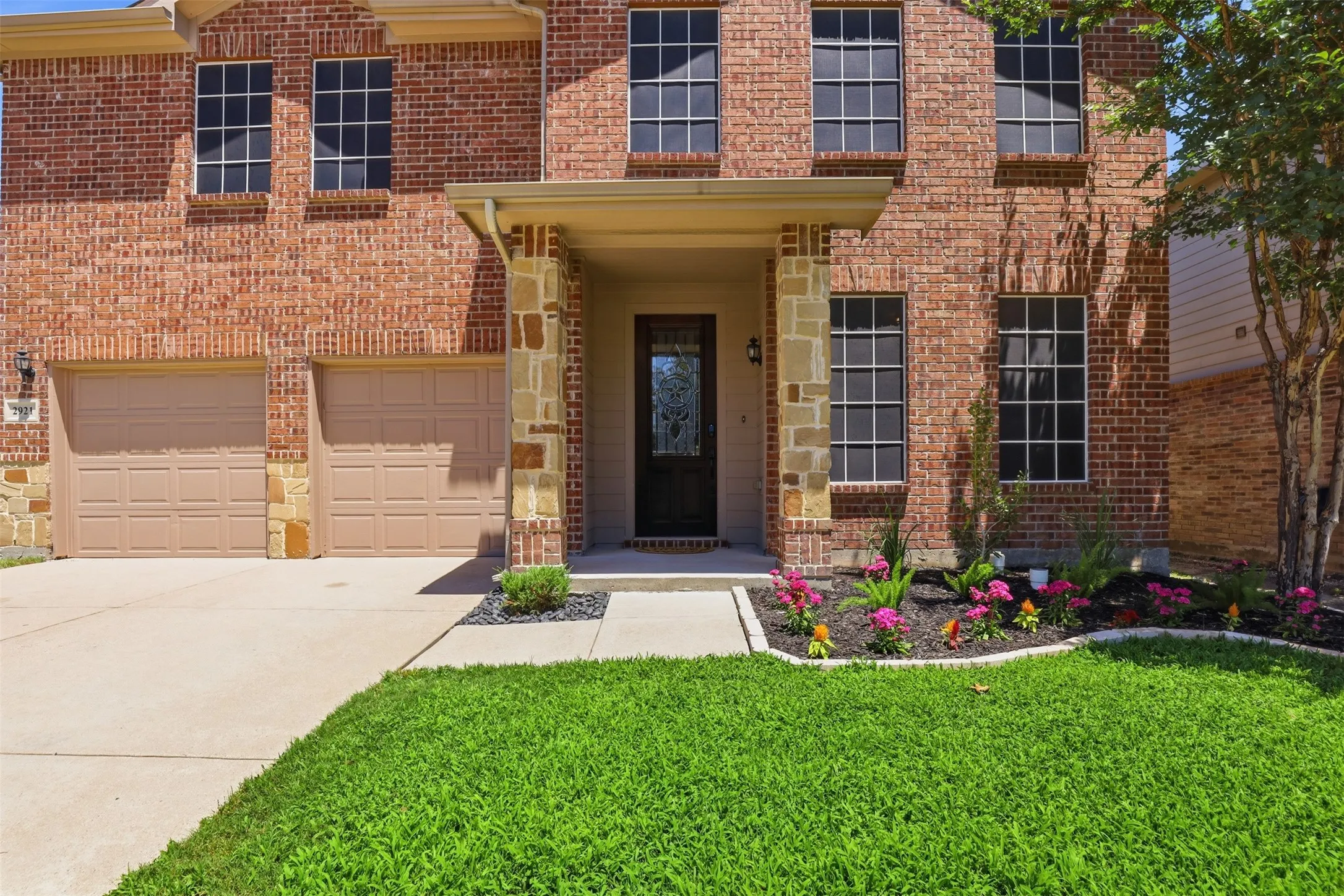 Brick and stone facade featuring a covered entry, decorative landscaping, two-car garage, and multiple windows