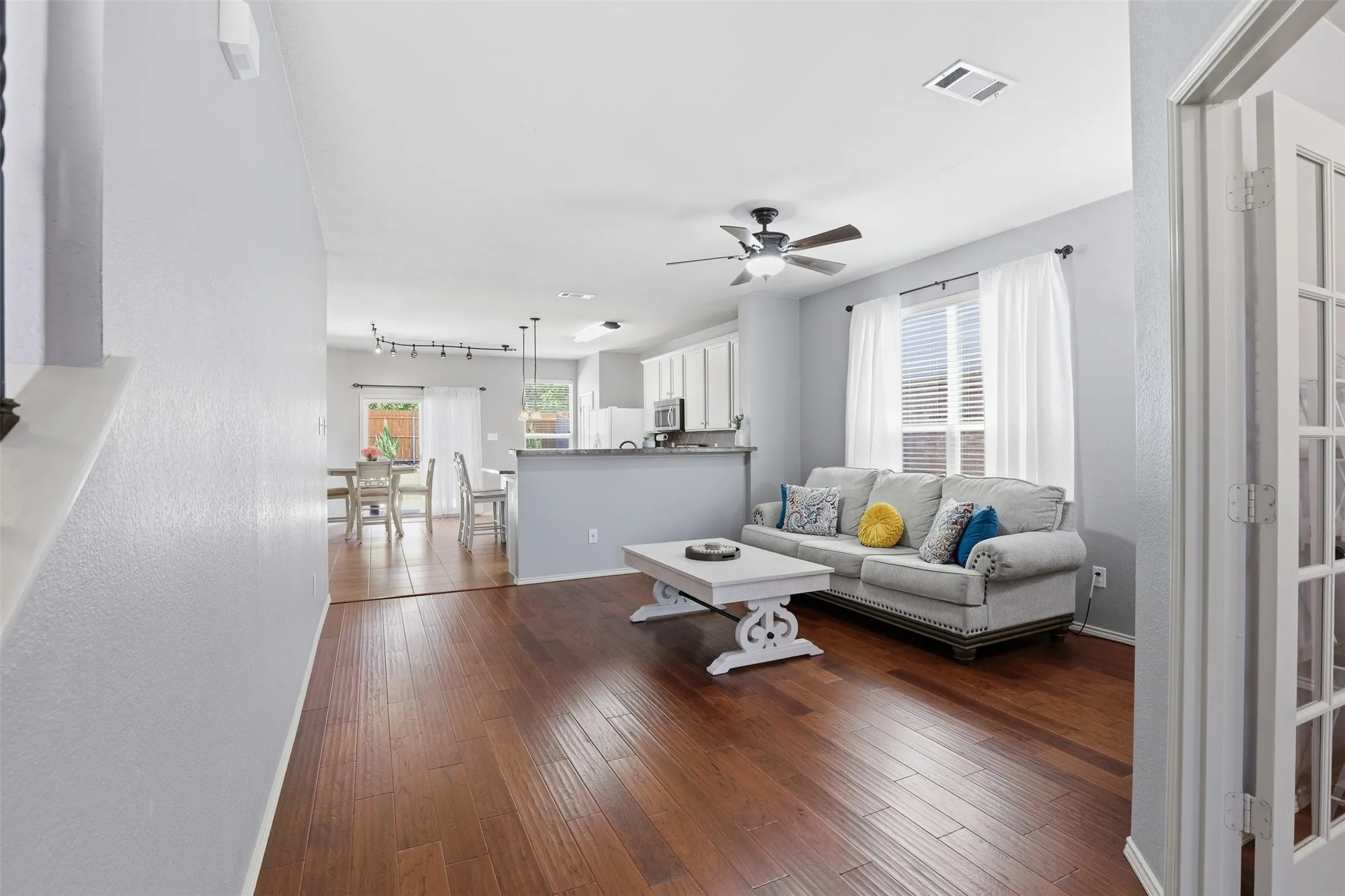 Open-concept living space featuring wood-finish flooring, a ceiling fan, and large windows with blinds