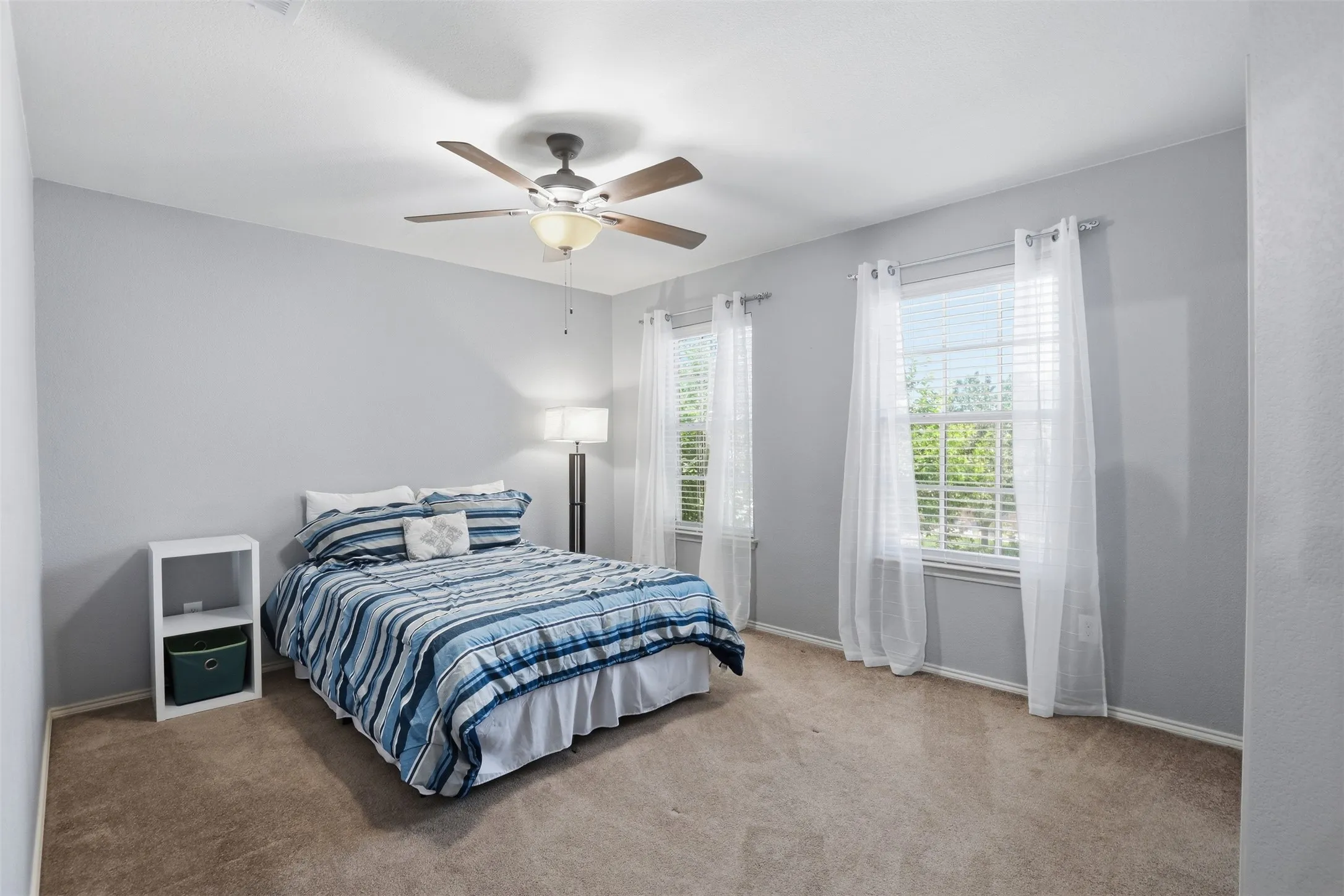 Spacious bedroom with large walk in closet featuring a ceiling fan with integrated lighting, and two windows providing abundant natural light
