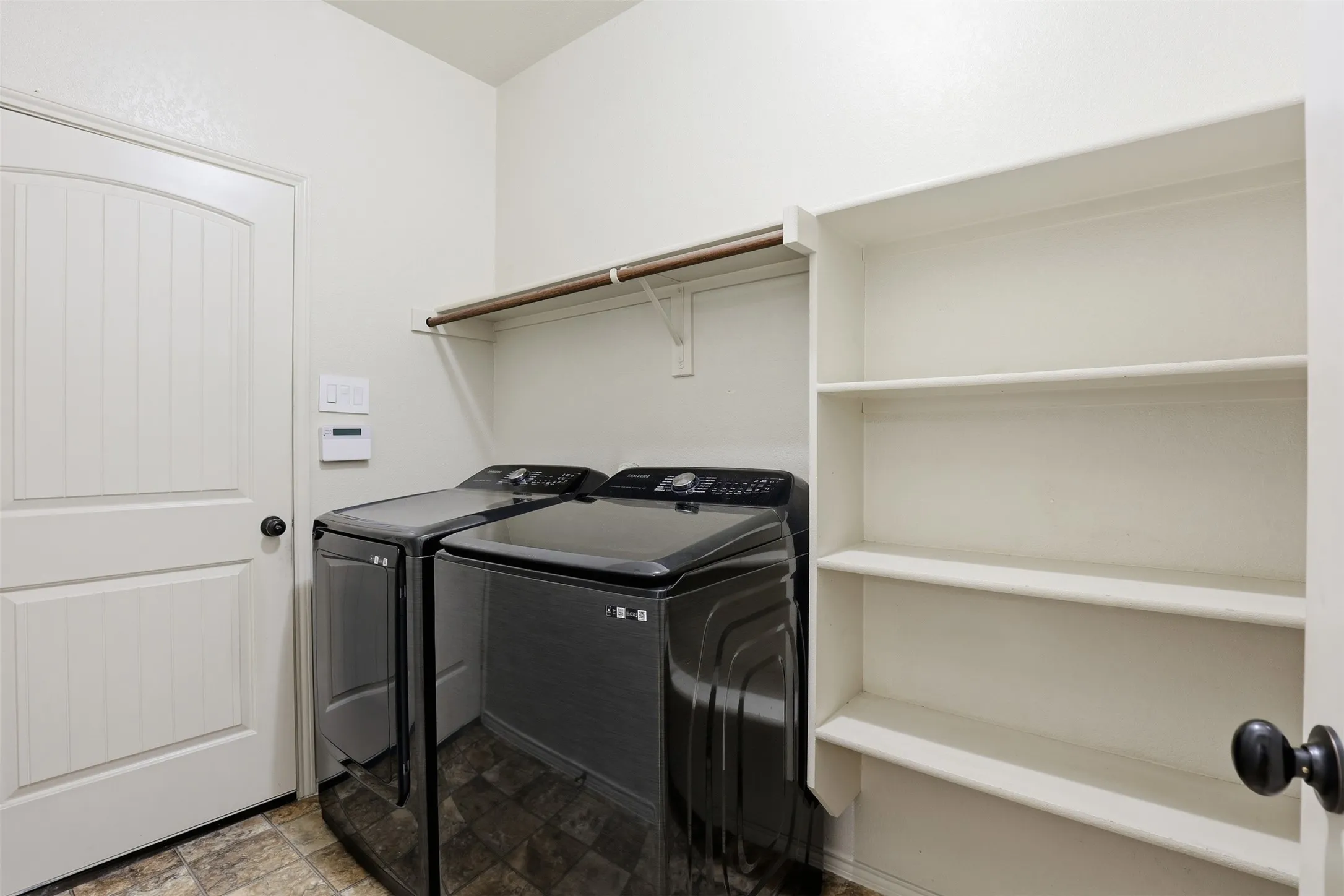 Dedicated laundry space featuring a white paneled door, built-in shelving, and a hanging rod