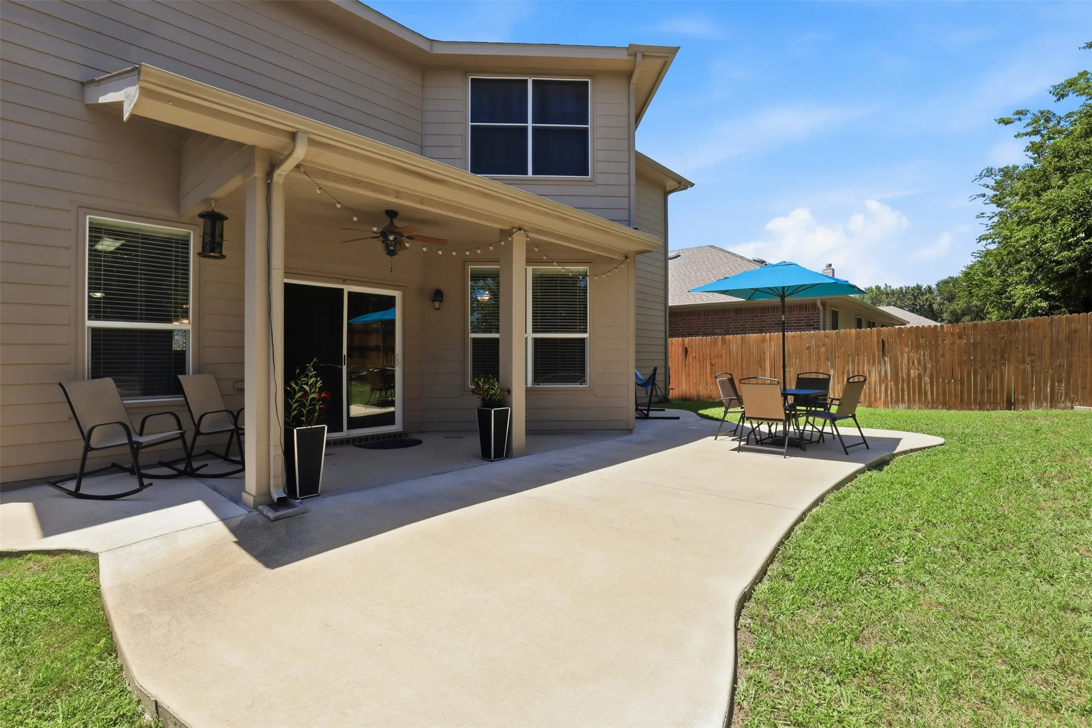 Expansive backyard featuring a covered patio, concrete pathway, and a privacy fence