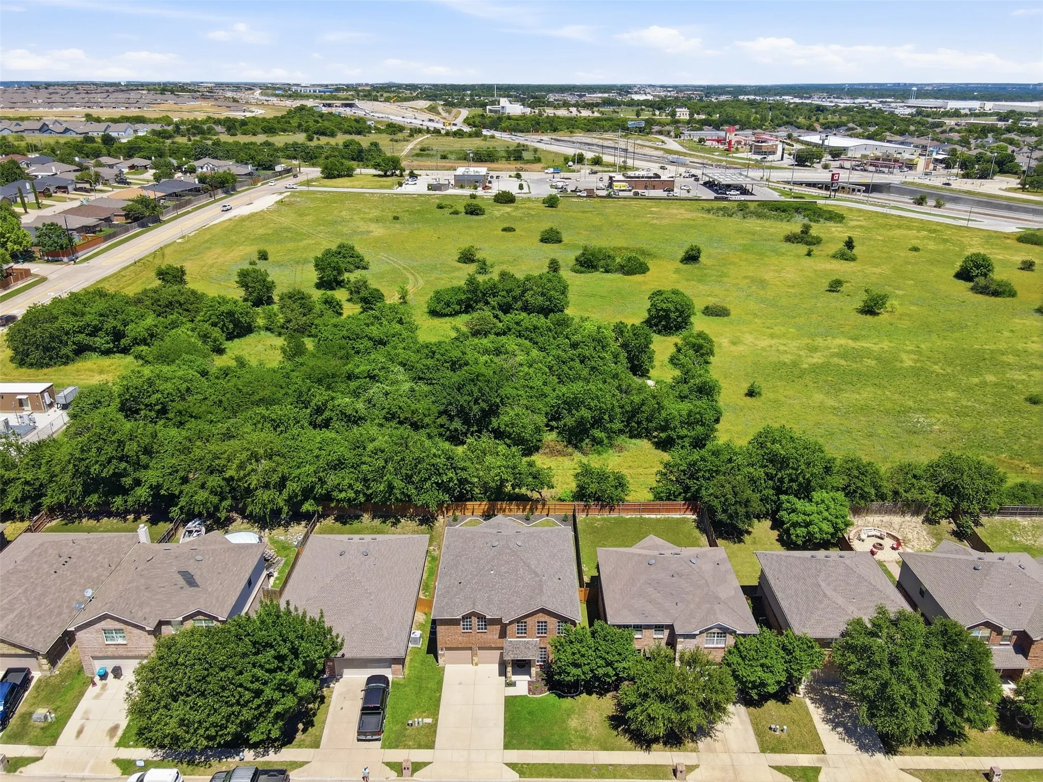 Aerial perspective showcasing a residential street with single-family homes, each featuring a private driveway and attached garage that backs up to wooded acreage