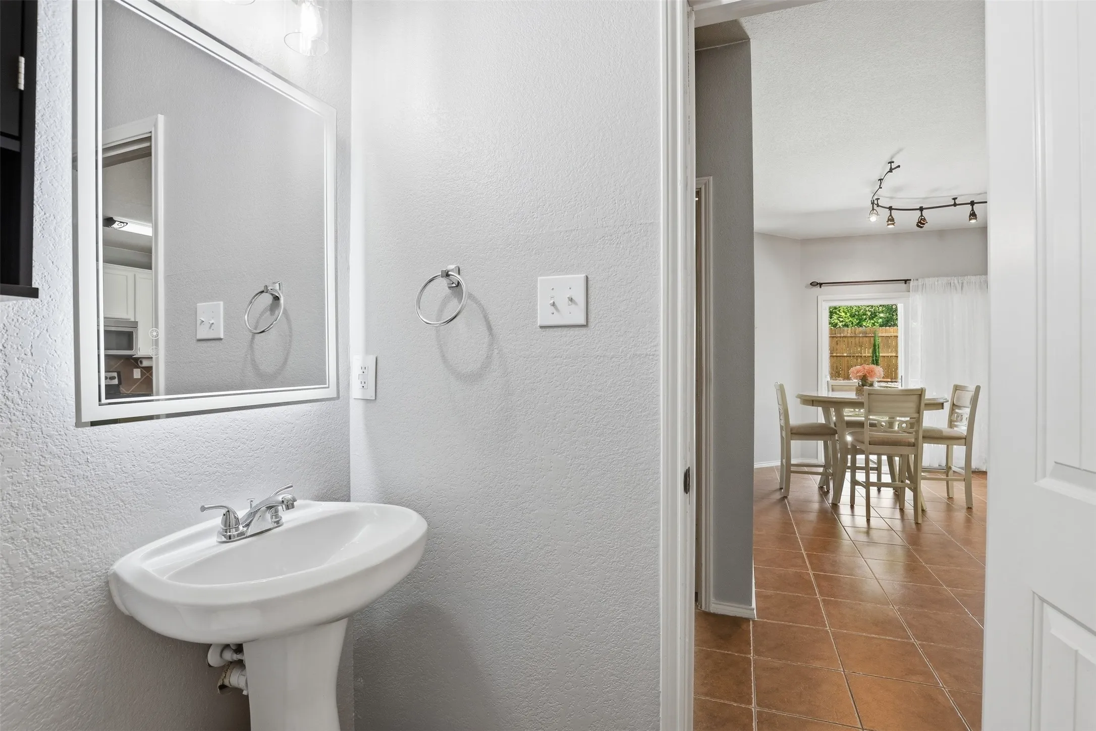 Downstairs 1/2 bath with pedestal sink with chrome faucet, framed mirror, and overhead vanity lighting