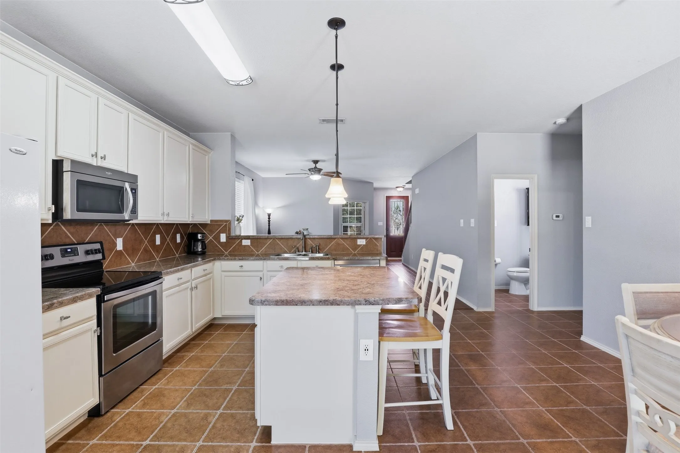 Open-concept kitchen featuring white cabinetry, stainless steel appliances, a tile backsplash, an island with seating, and tile​​‌​​​​‌​​‌‌​‌‌​​​‌‌​‌​‌​‌​​​‌​​ flooring