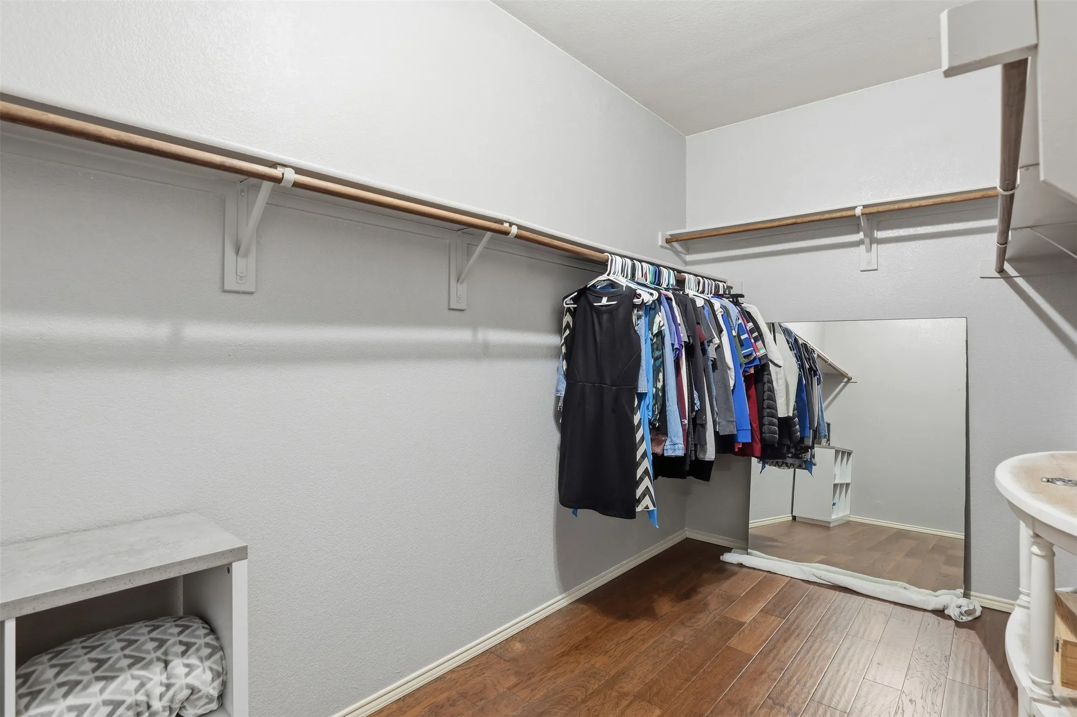 Primary walk-in closet located on the 1st floor featuring wood-finish flooring, multiple hanging rods, built-in shelving, and light gray walls