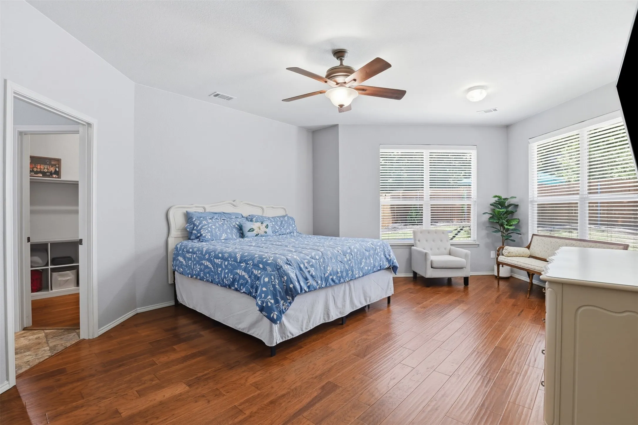 Spacious primary bedroom located on the 1st floor featuring wood-finish flooring, light grey wall paint, and multiple windows with blinds