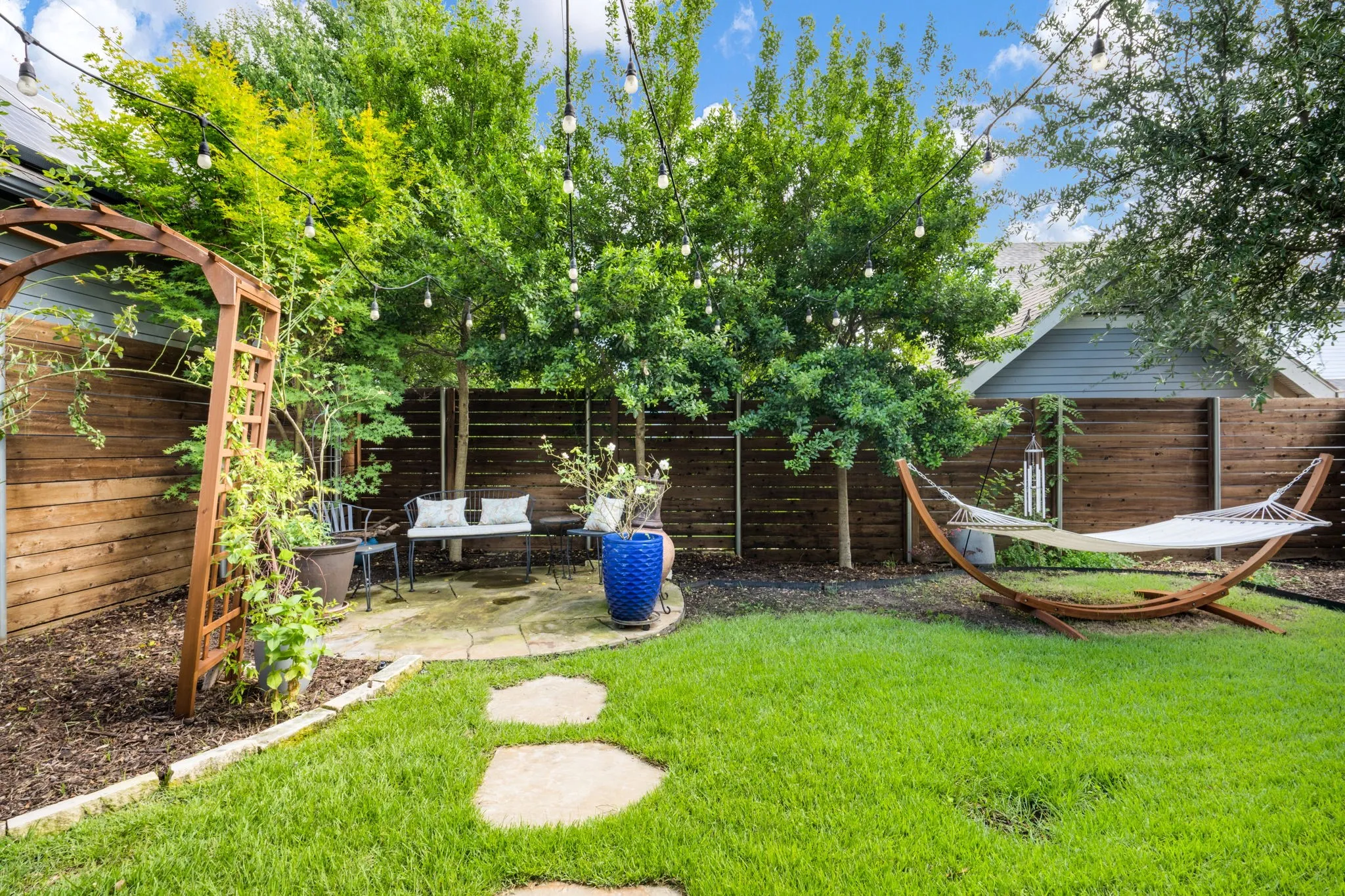     Private backyard retreat with lush landscaping, string lighting, and hammock lounge area.