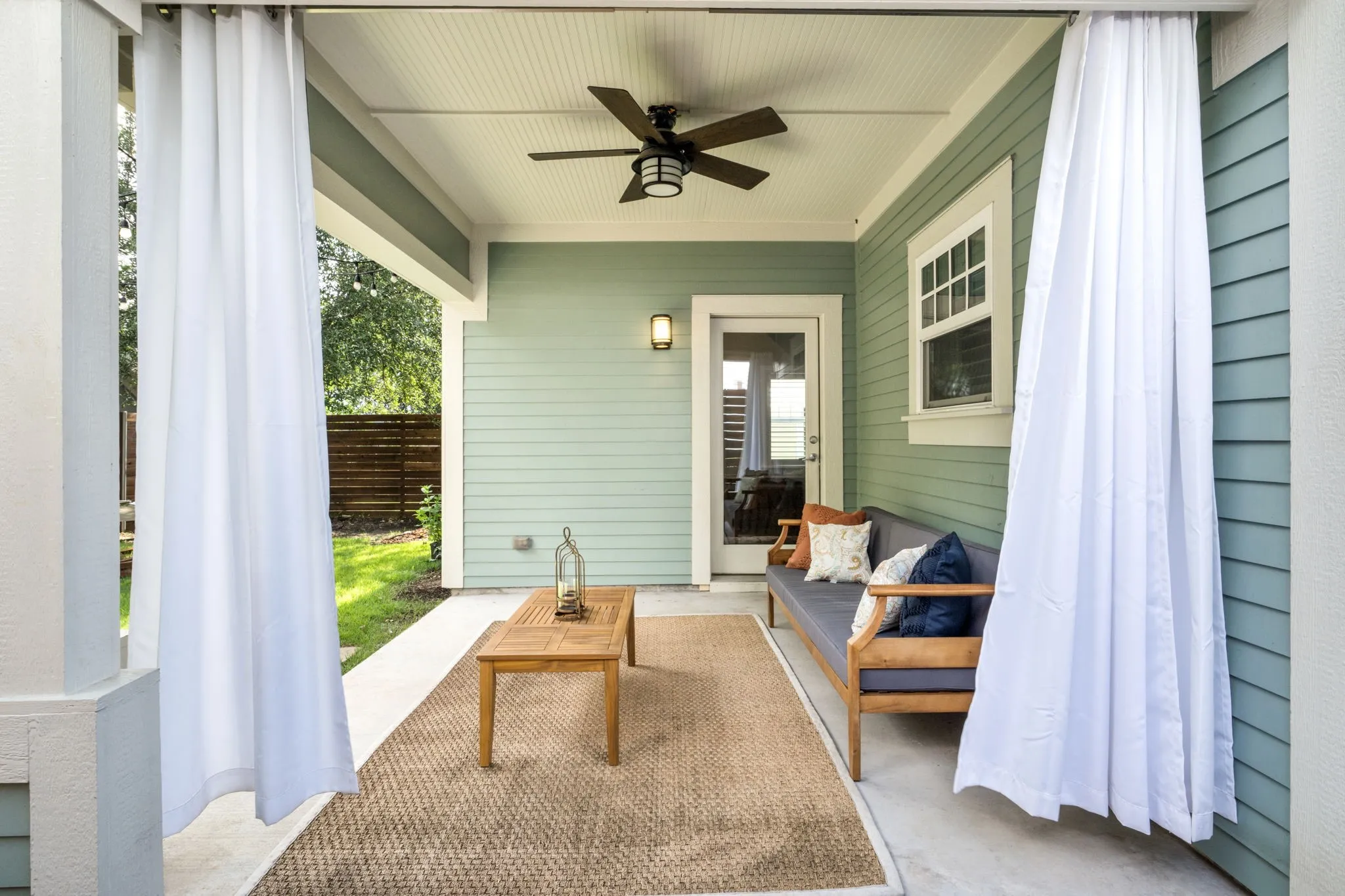     Covered patio with ceiling fan and cozy seating area overlooking the landscaped backyard.