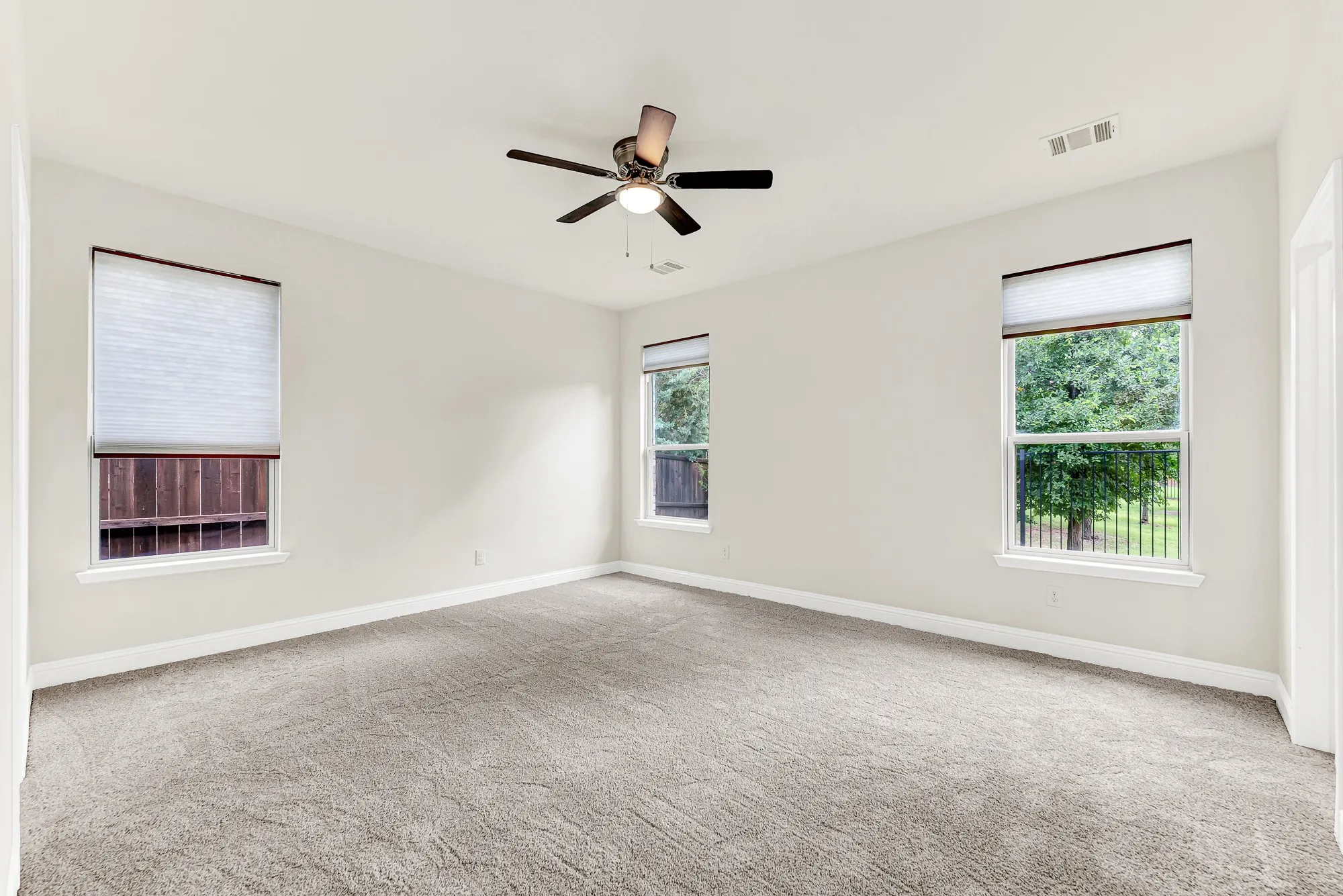 The triple-window arrangement creates a symmetrical anchor, bathing the neutral floors in soft, natural light. This peaceful sanctuary invites you to disconnect at the end of the day and watch the evening shadows stretch across the room