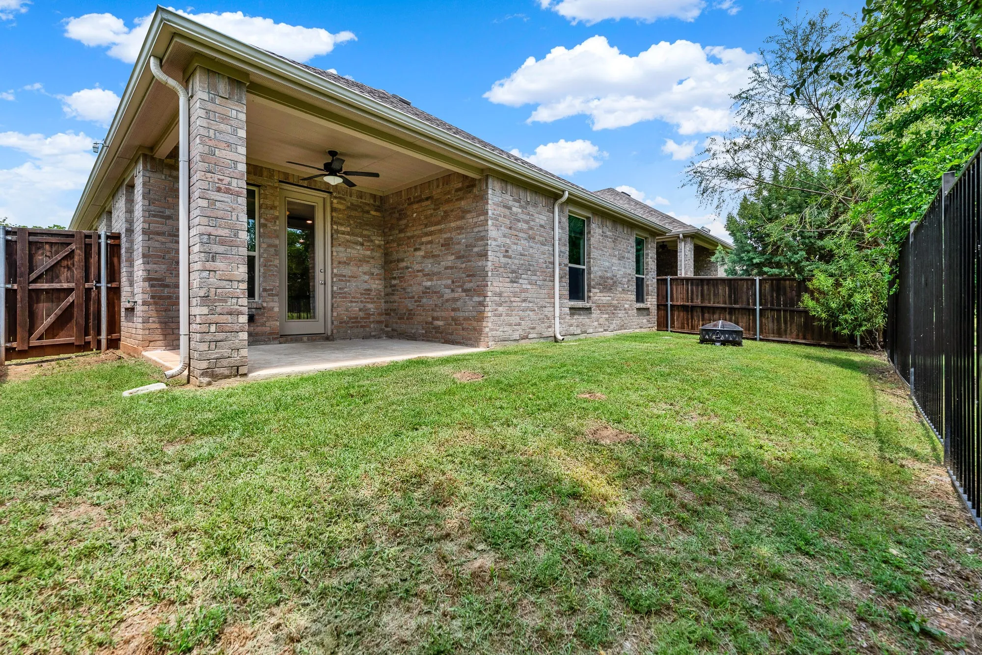 A deep-set porch roof, complete with a dark ceiling fan, casts a welcoming shadow across the expansive brick exterior. This breezy alcove invites you to host casual weekend barbecues where guests can easily mingle between the indoor kitchen and the grassy lawn.