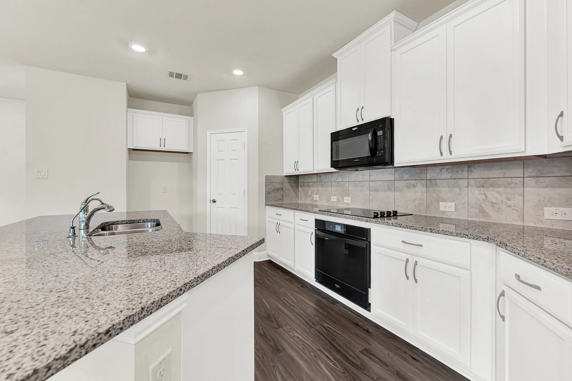 The long stretch of polished granite countertop beautifully reflects the soft glow of recessed ceiling lights. Here, you will love the ease of prepping a fresh weeknight dinner with everything positioned right at your fingertips