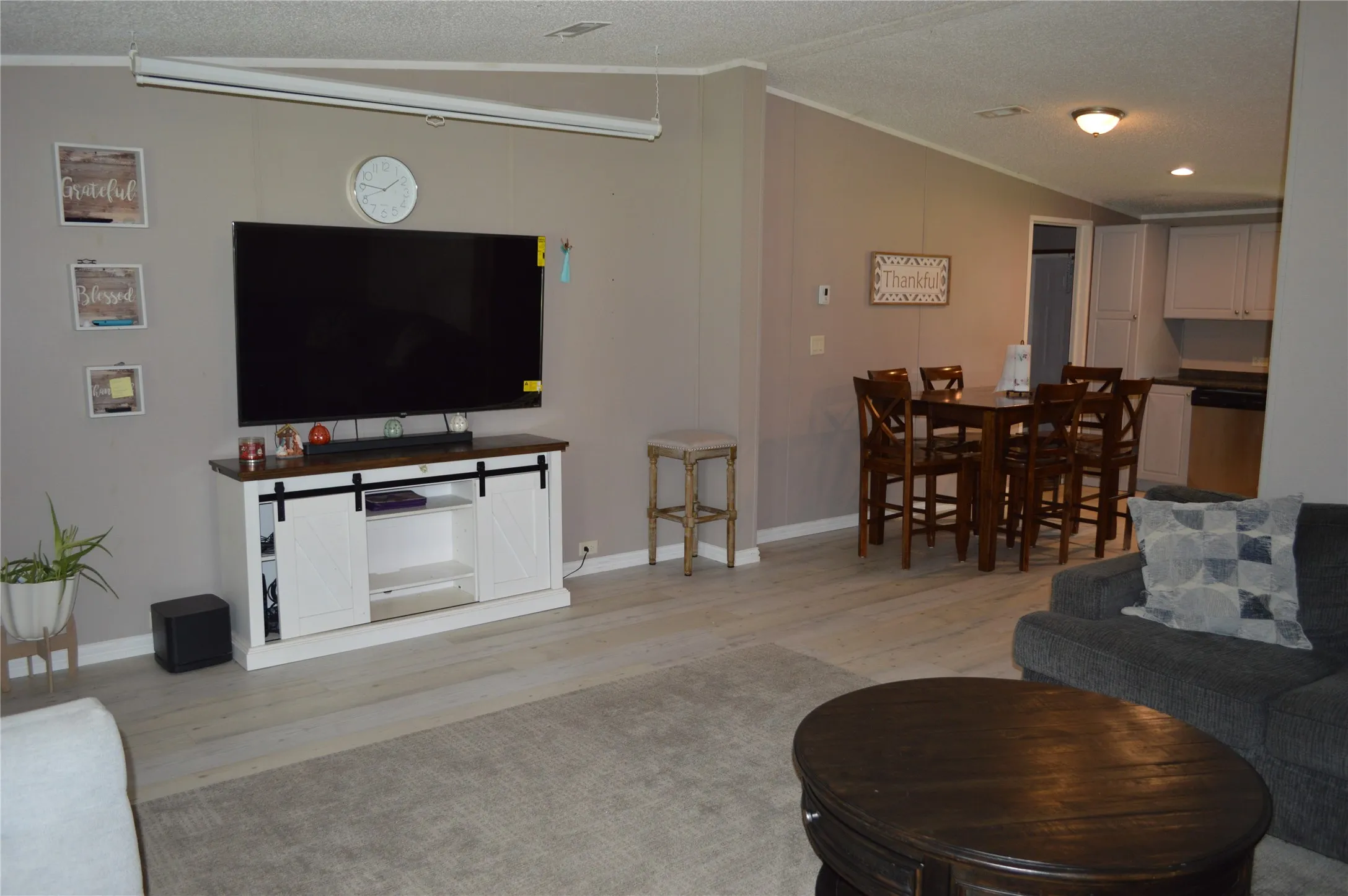 Open-concept living area featuring light wood-finish flooring, a neutral wall color, and a dining area with a wood table and chairs