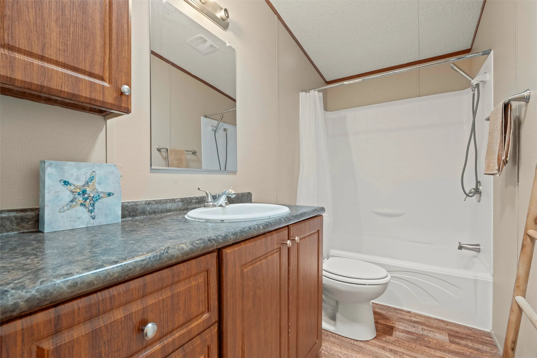 Bathroom featuring a built-in wood-finish vanity with a single basin sink, laminate countertop, and overhead storage cabinetry