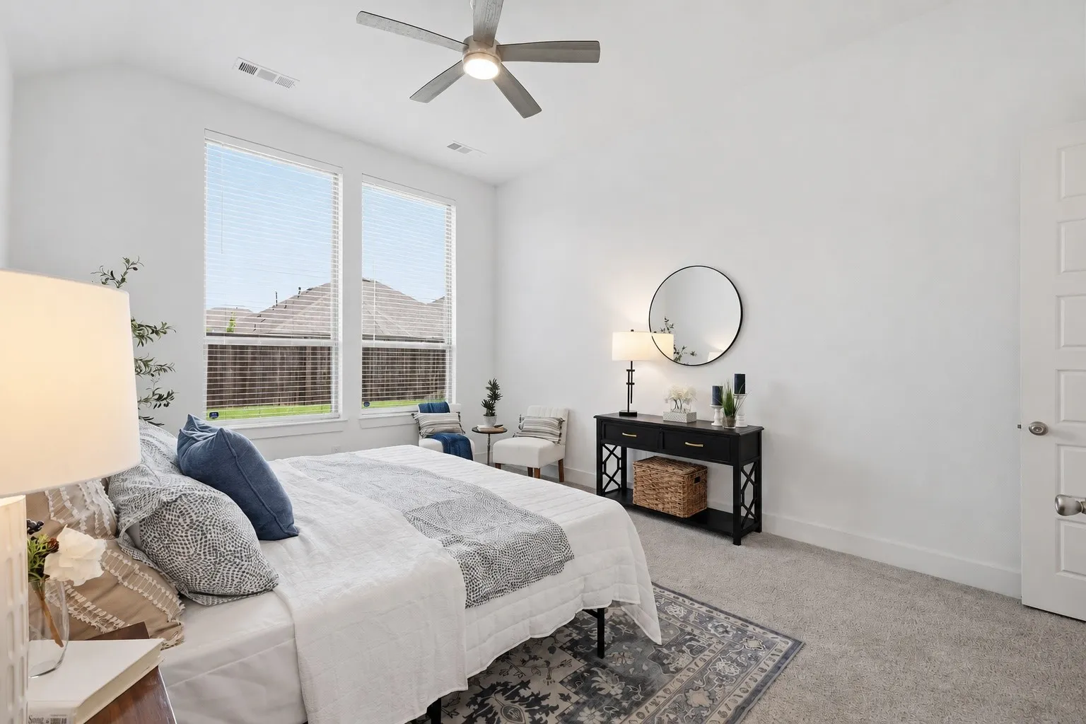 Bright bedroom featuring large windows, neutral carpet flooring, a ceiling fan with integrated lighting, and white walls