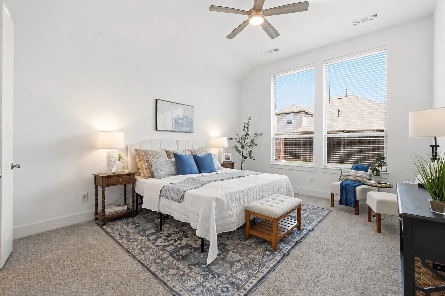 Spacious room featuring vaulted ceilings, ample natural light from two large windows, soft carpet flooring, and a ceiling fan