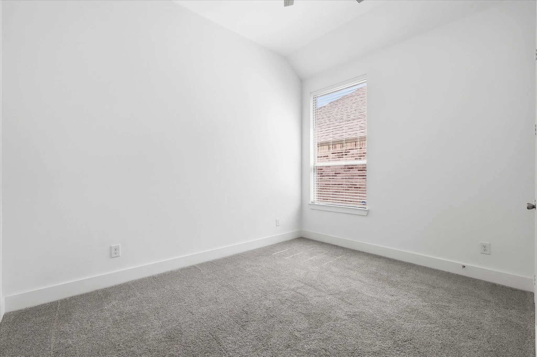 Carpeted interior room with white walls, a single window with blinds, and white baseboards