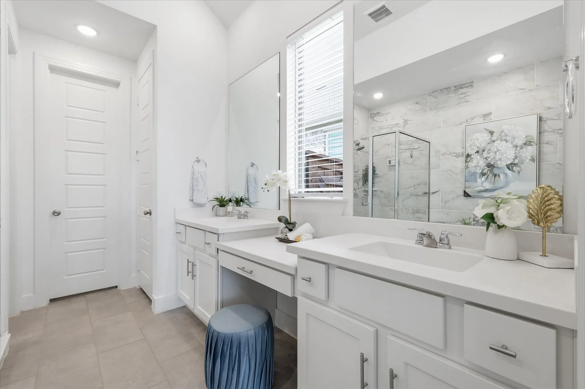 Spacious bathroom featuring dual white vanities with integrated sinks, ample counter space, a dedicated makeup area, and large format tile flooring