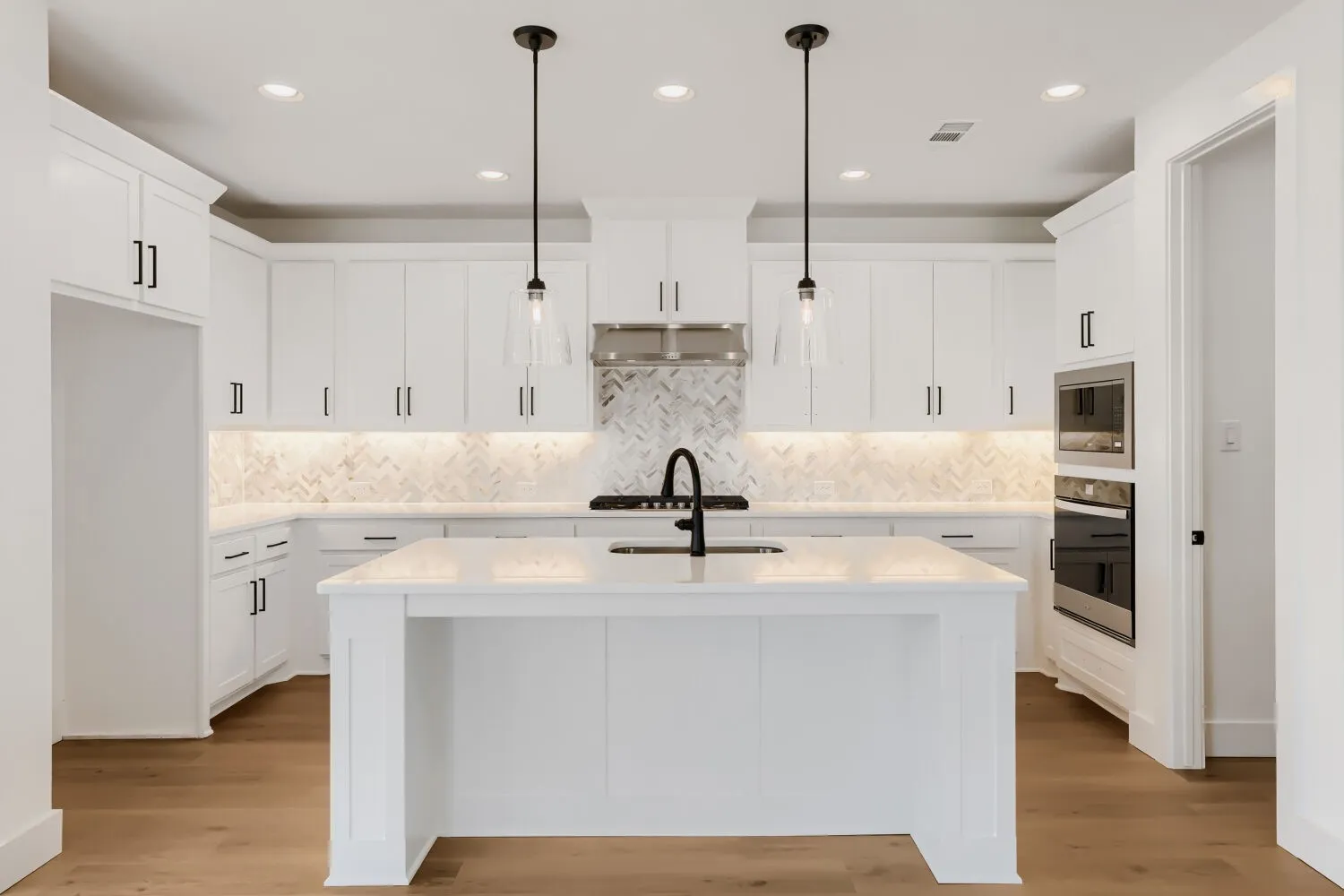 Kitchen featuring white cabinetry, a large center island, built-in stainless steel appliances, a chevron pattern backsplash, and wood-finish flooring
