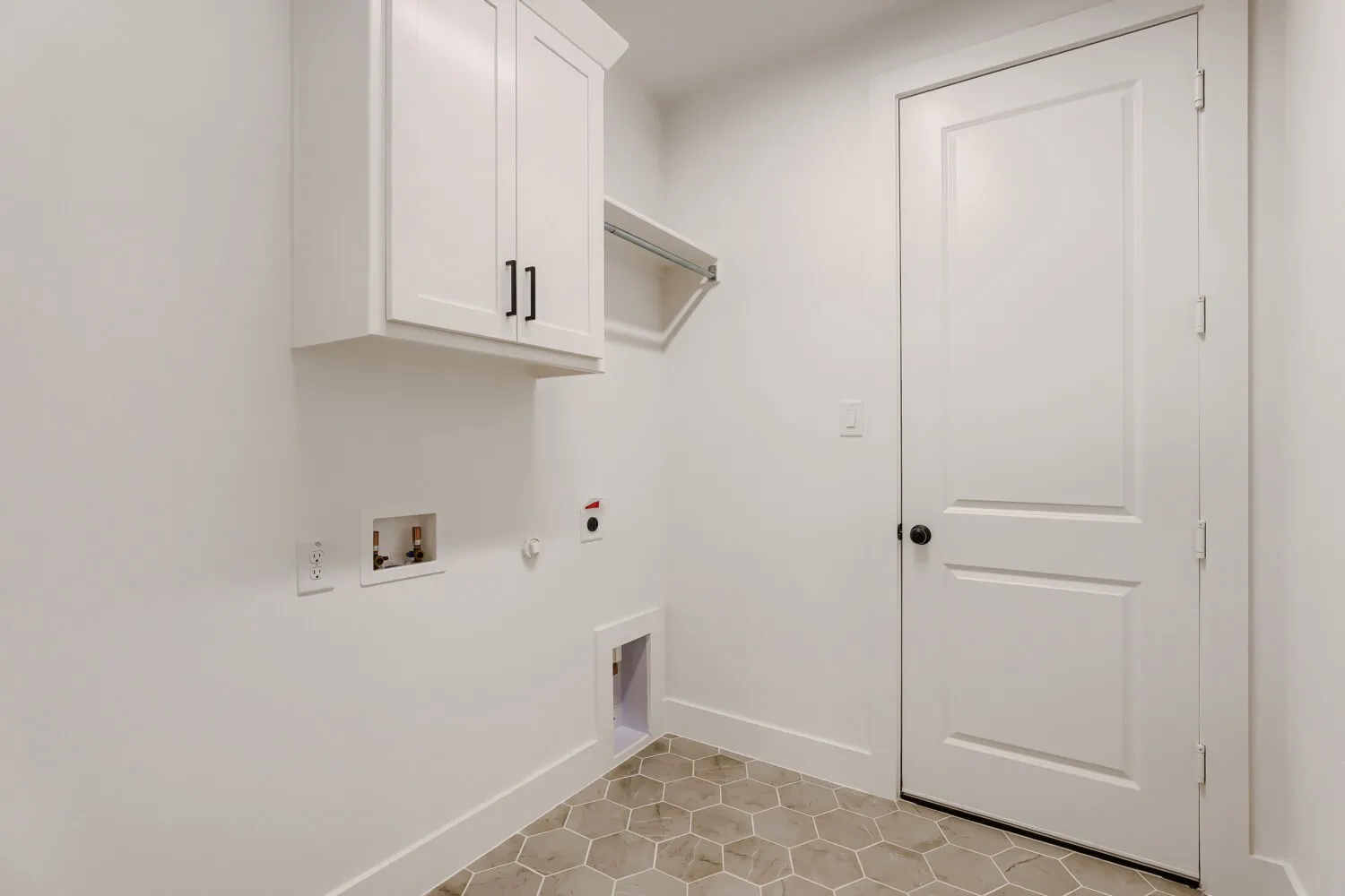Hexagonal floor tiling, white shaker-style cabinetry, black cabinet hardware, white interior door, and a built-in hanging rod