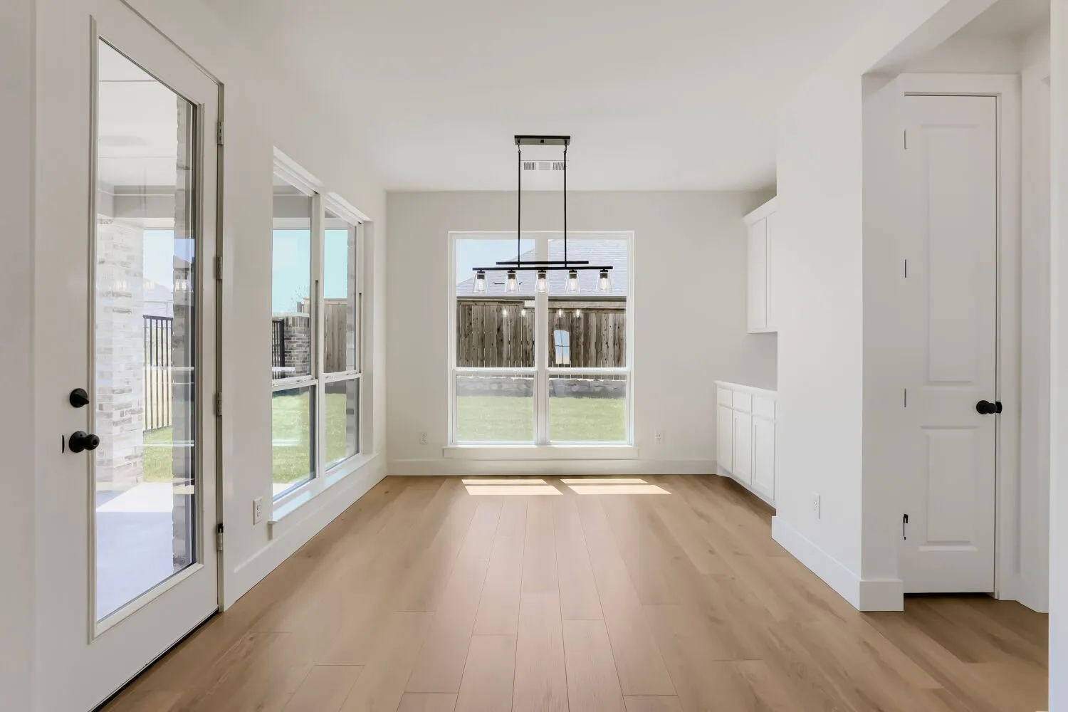 Wood-finish flooring throughout, white cabinetry, a glass-paneled exterior door, and a multi-light linear chandelier