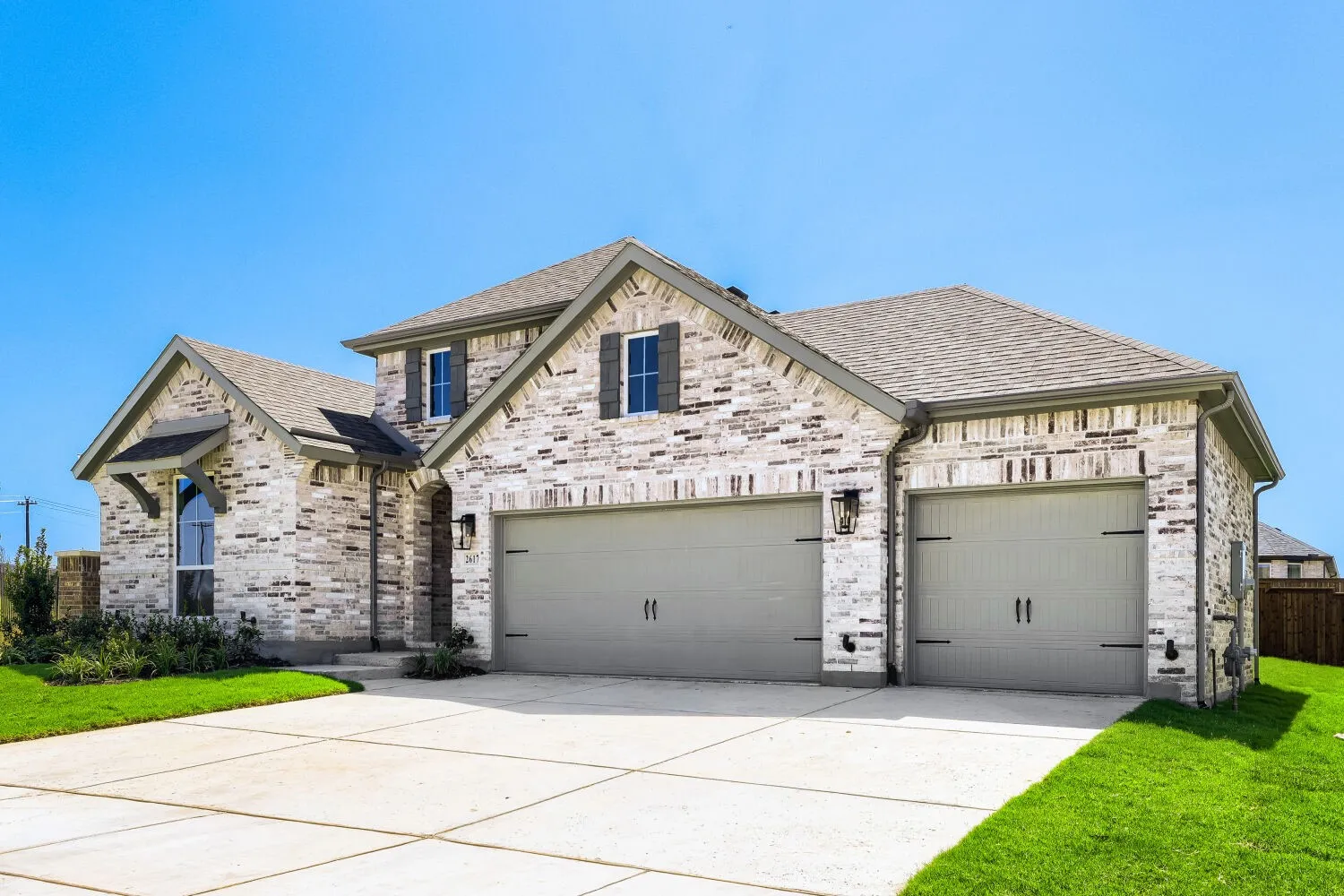 Brick veneer facade with gabled roof lines, attached two-car garage, concrete driveway, and established green lawn