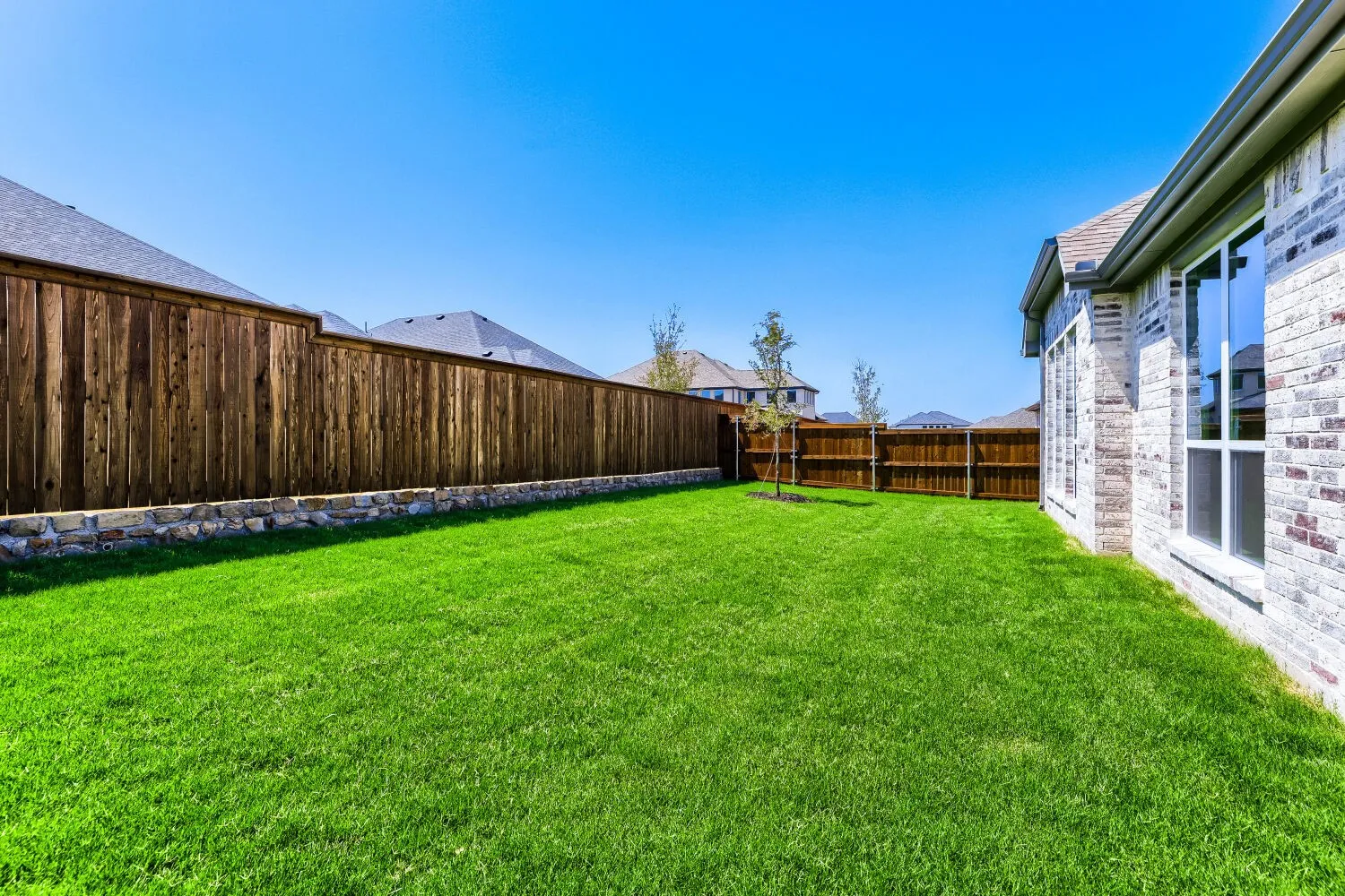 Expansive grassy yard with full wood fencing and a stone base
