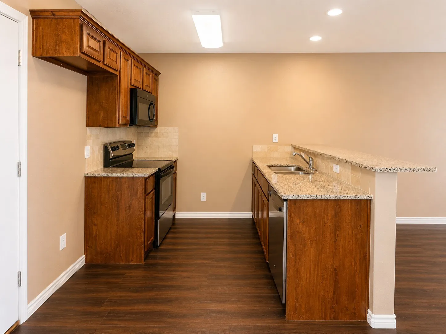 Kitchen featuring wood-finish cabinetry, light speckled countertops, stainless steel appliances, and wood-finish flooring