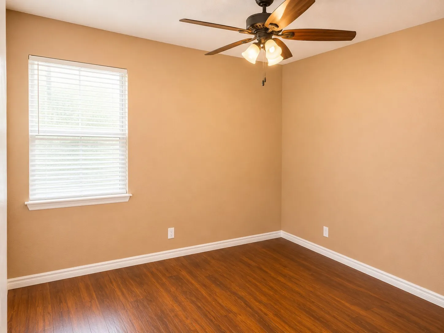 Room with wood-finish flooring, a ceiling fan with light fixture, and a window with white blinds