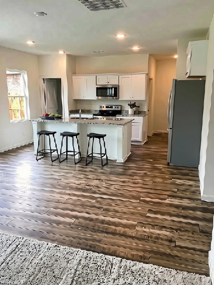 Spacious kitchen featuring white cabinetry, stainless steel appliances, an island with countertop seating, recessed lighting, and wood-finish flooring