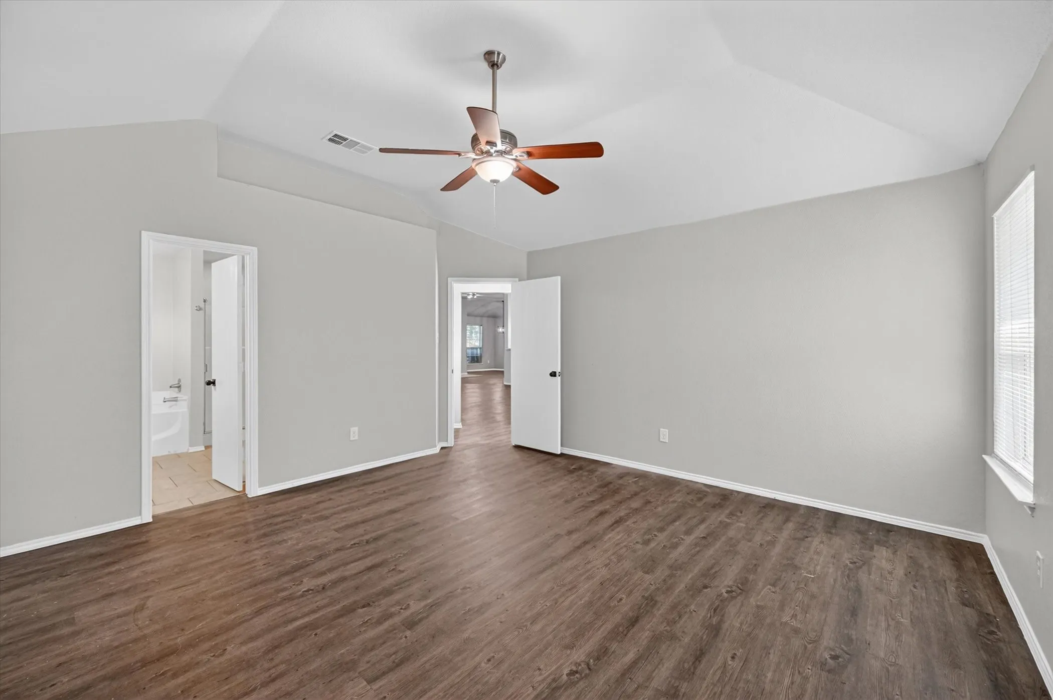 Spacious room featuring vaulted ceilings, wood-finish flooring, a ceiling fan with light fixture, and neutral wall tones