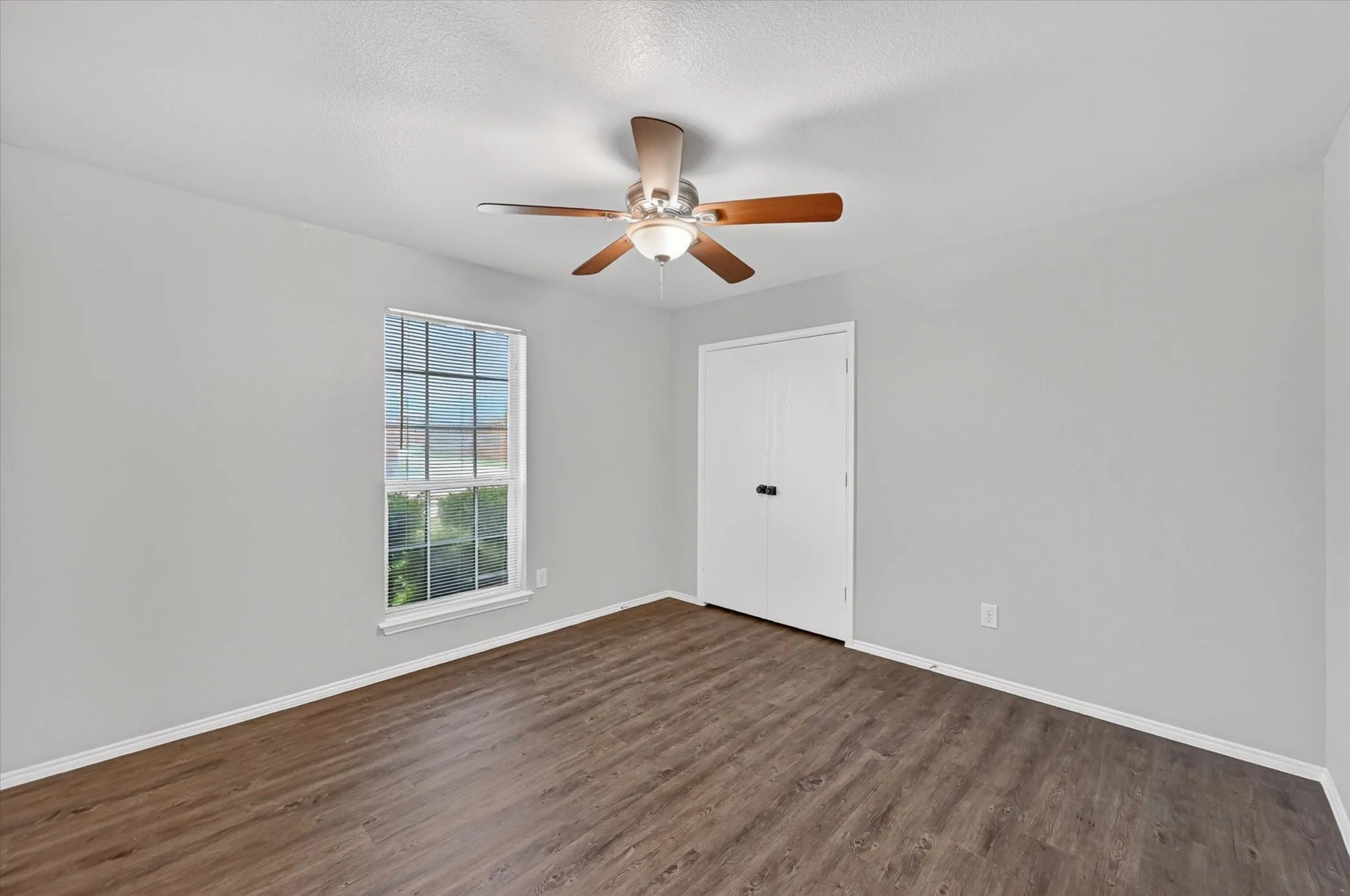 Room featuring wood-finish flooring, a window with grid panes, a ceiling fan with integrated lighting, and a bi-fold closet door