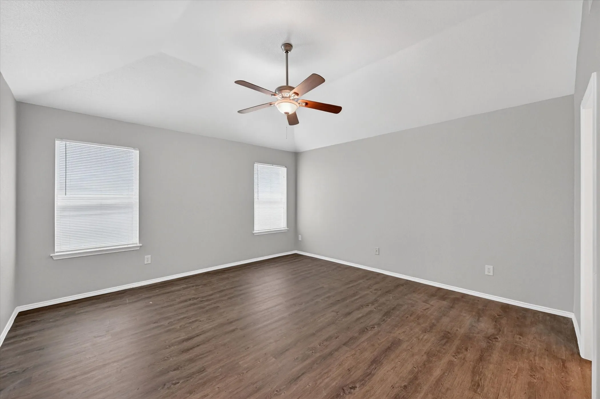Spacious room featuring vaulted ceilings, wood-finish flooring, and two windows with blinds