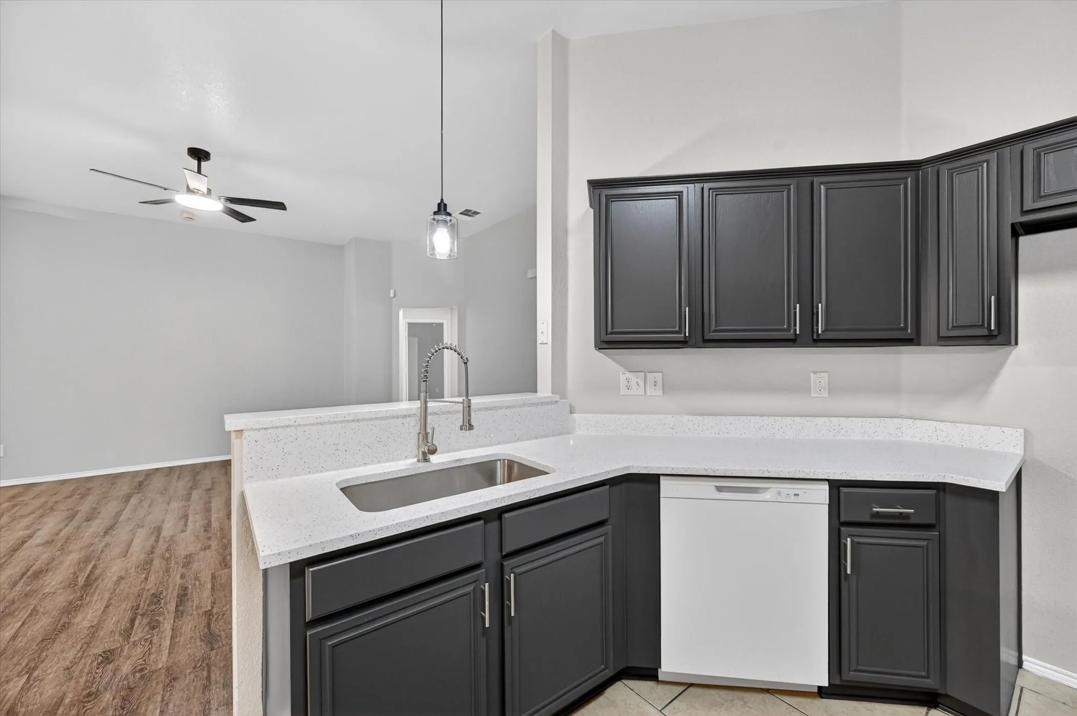 Kitchen featuring dark gray cabinetry, white speckled countertops, an undermount stainless steel sink, and a modern pendant light fixture
