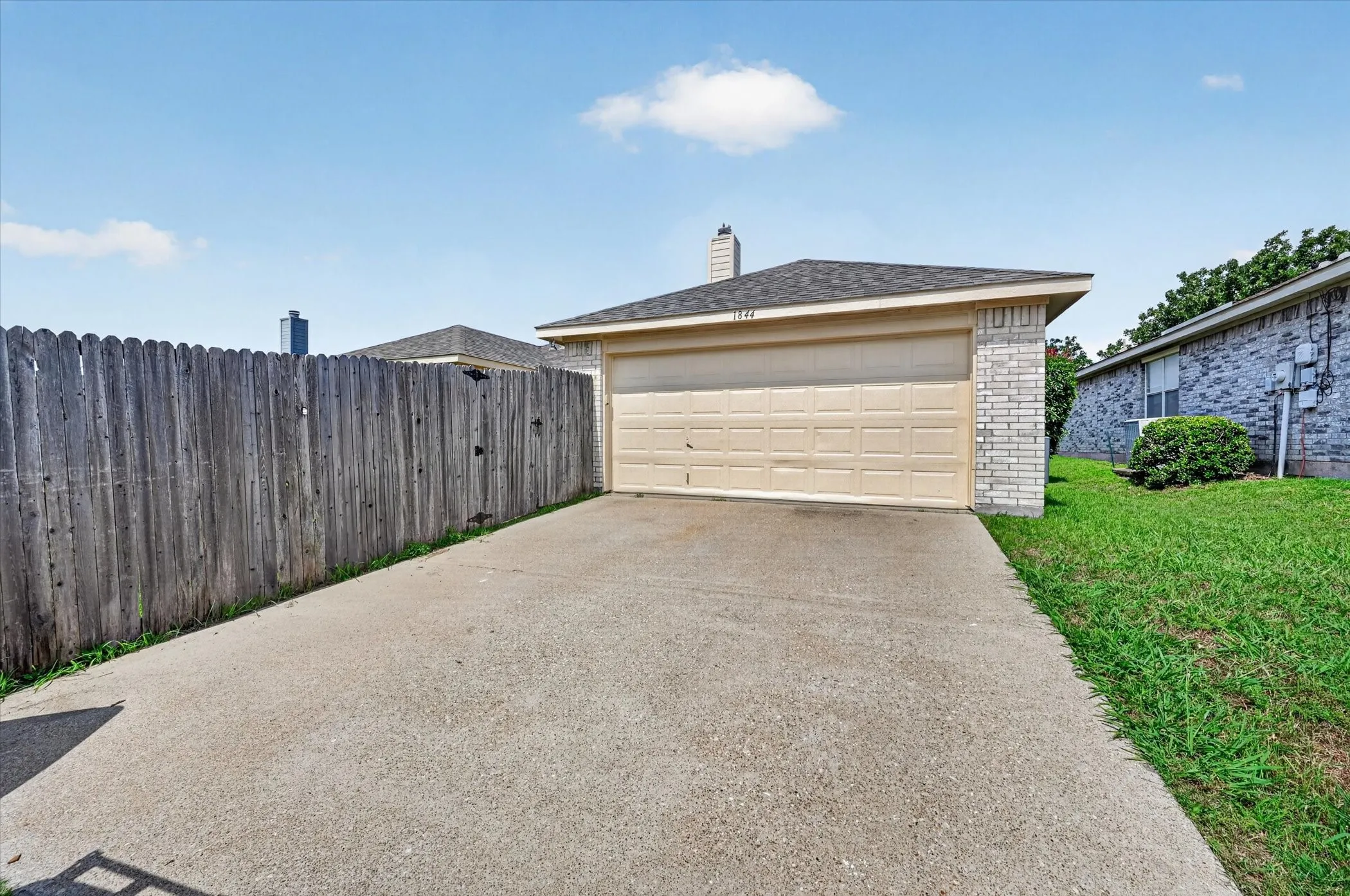 Attached garage with a tan overhead door, light brick accents, and a dark shingled roof