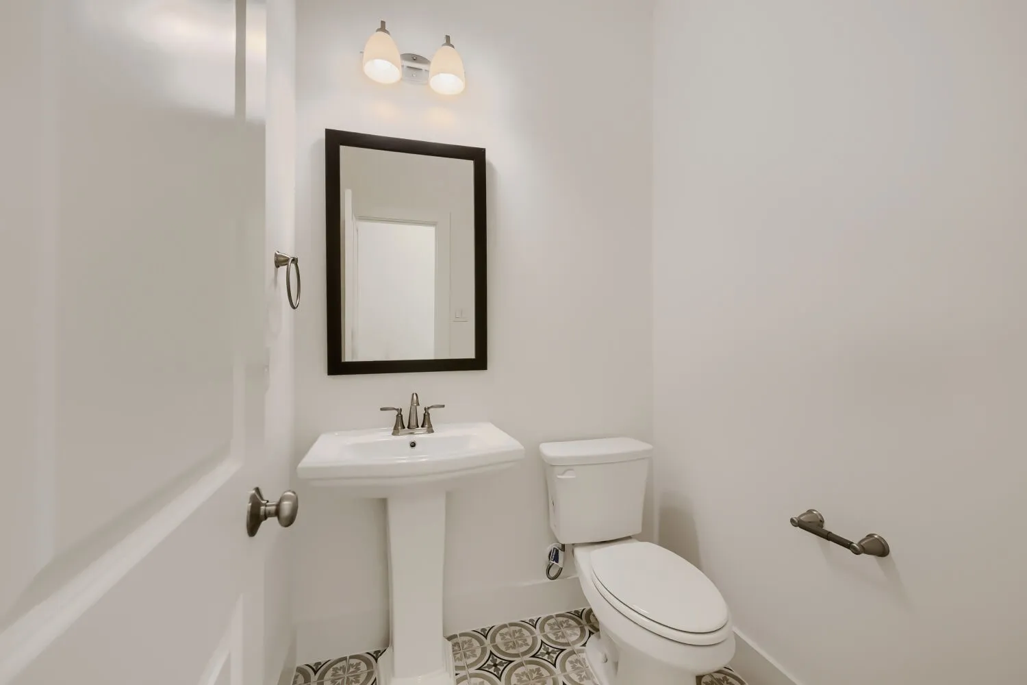 Powder room featuring a pedestal sink with a chrome faucet, a rectangular framed mirror, and decorative floor tiling