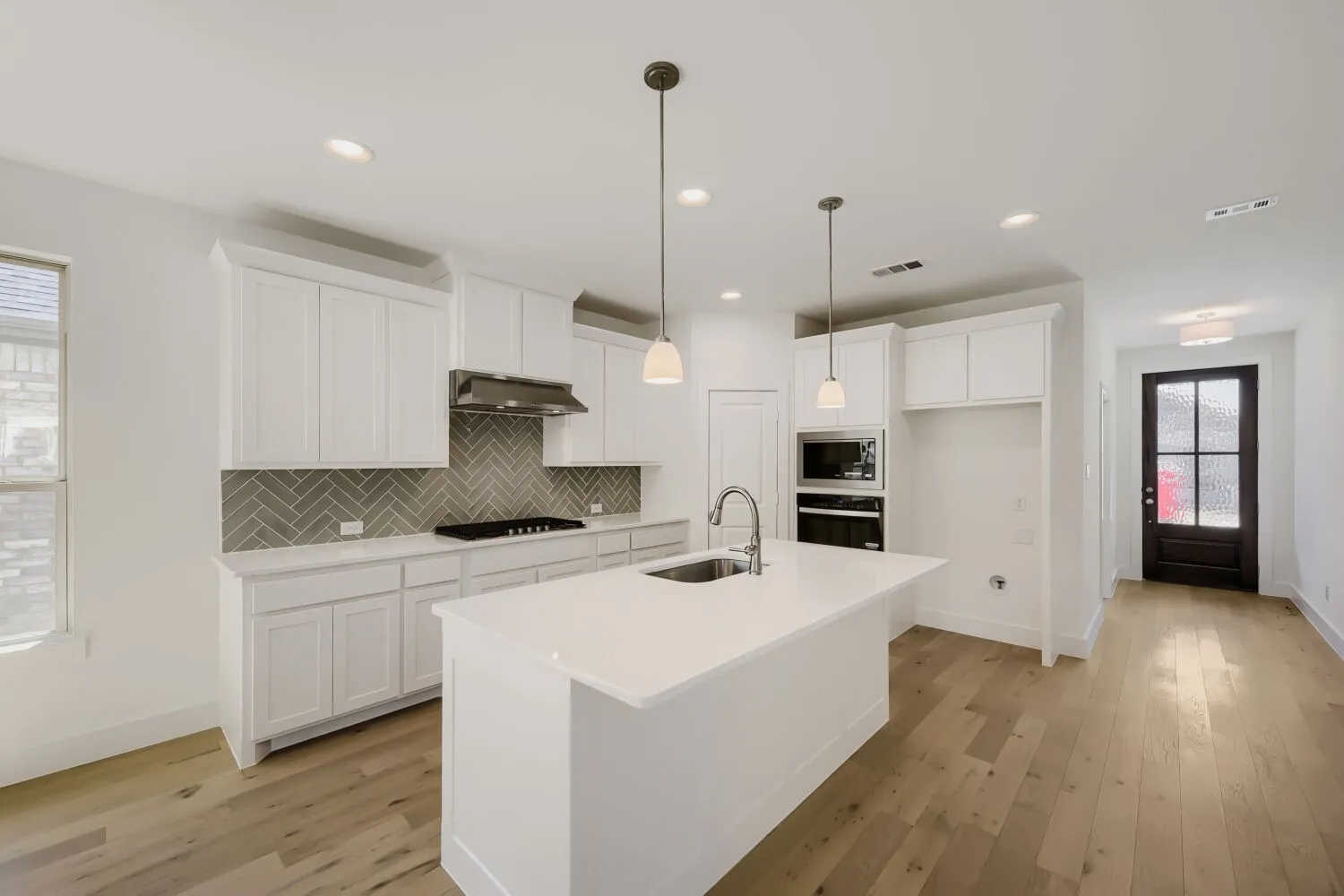 Modern kitchen featuring an expansive center island with an undermount sink, white cabinetry, herringbone tile backsplash, and wood-finish flooring