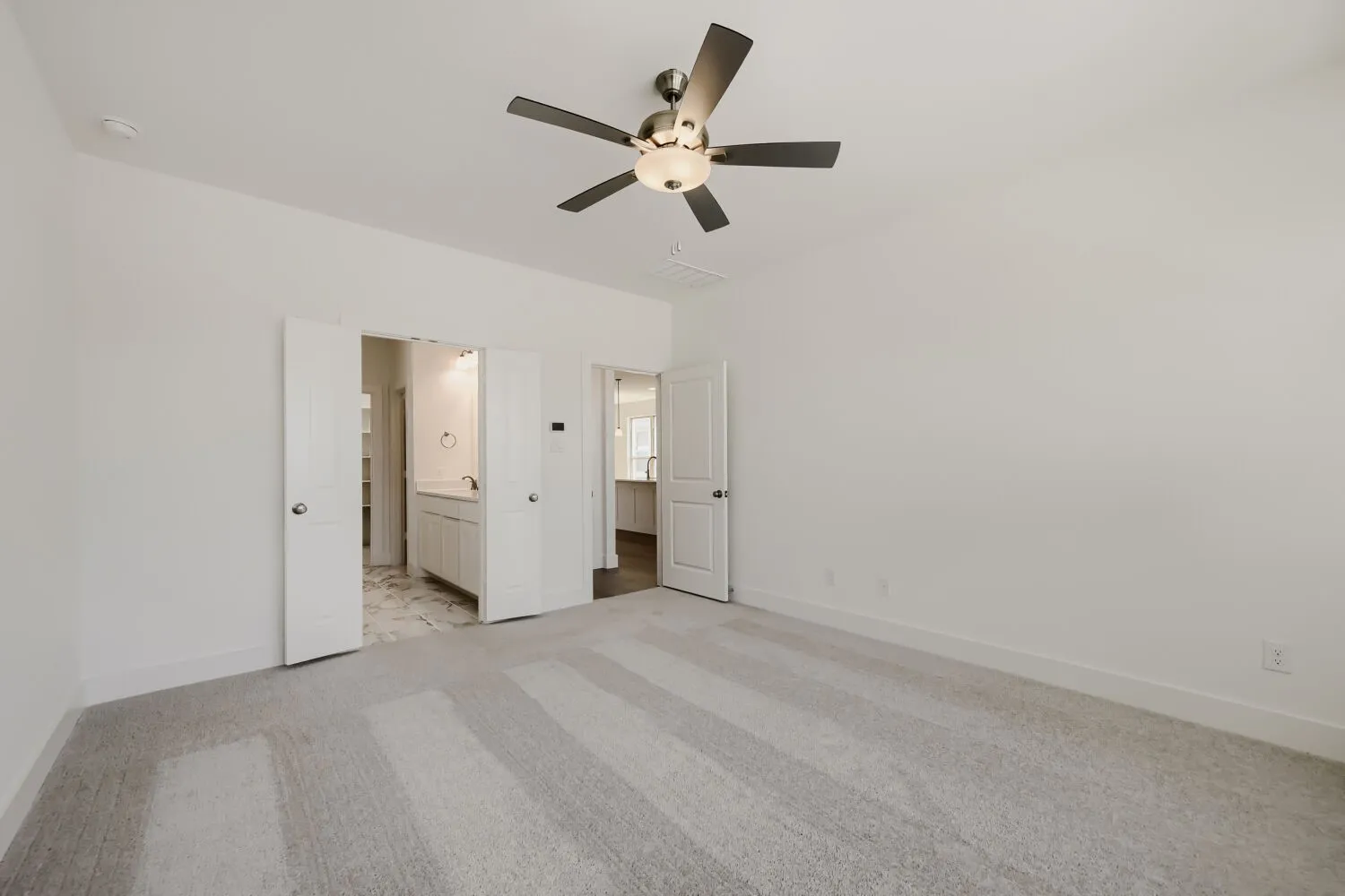 Spacious room featuring light gray patterned carpeting, a contemporary ceiling fan with integrated lighting, and crisp white walls