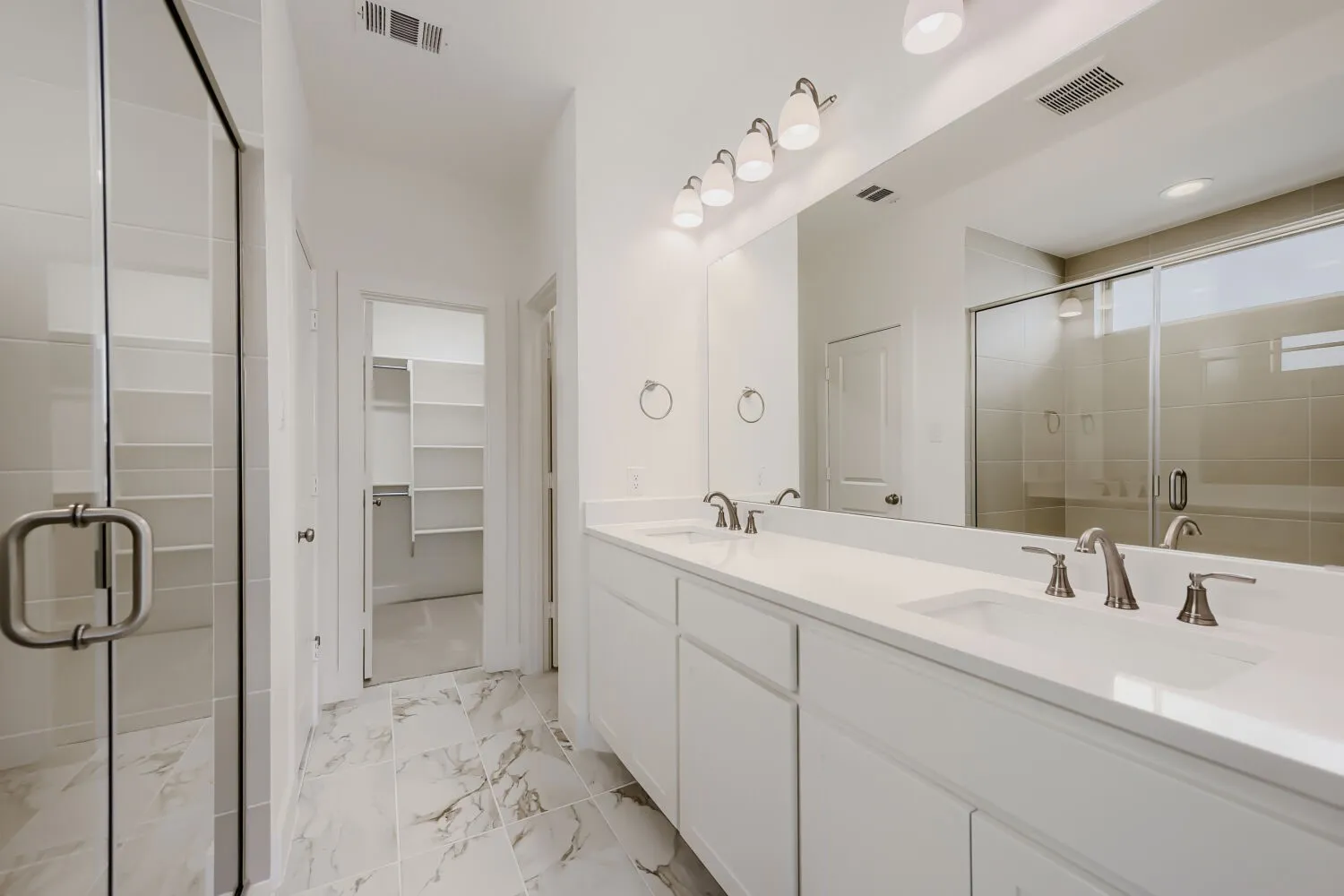 Spacious bathroom featuring a dual vanity with undermount sinks, a large mirror, and an enclosed shower with a glass door