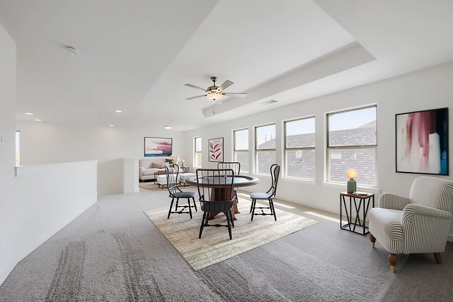Virtually Staged Photo - Bright, open upper-level living space featuring multiple large windows with natural light, ceiling fan with integrated lighting, and geometric wall art