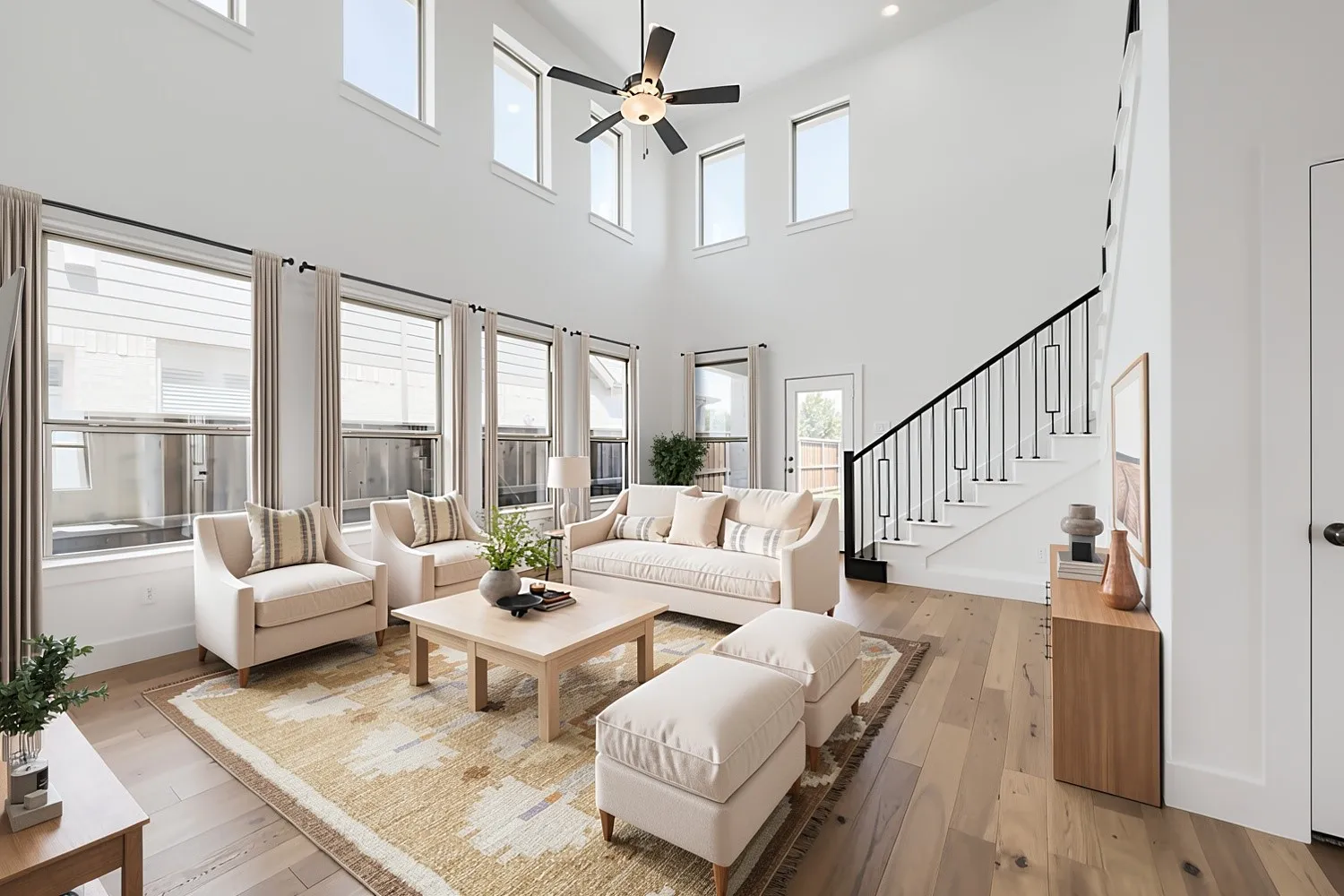 Virtually Staged Photo - High ceilings with upper transom windows, wood-finish flooring, staircase with custom metal railing, multiple large windows, and a ceiling fan