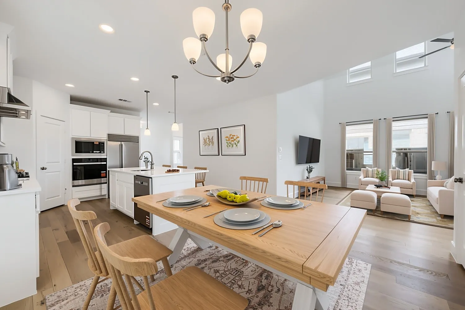 Virtually Staged Photo - Open-concept living area with wood-finish flooring, a two-story ceiling, and a kitchen featuring a center island with a built-in dishwasher, stainless steel appliances, and white cabinetry