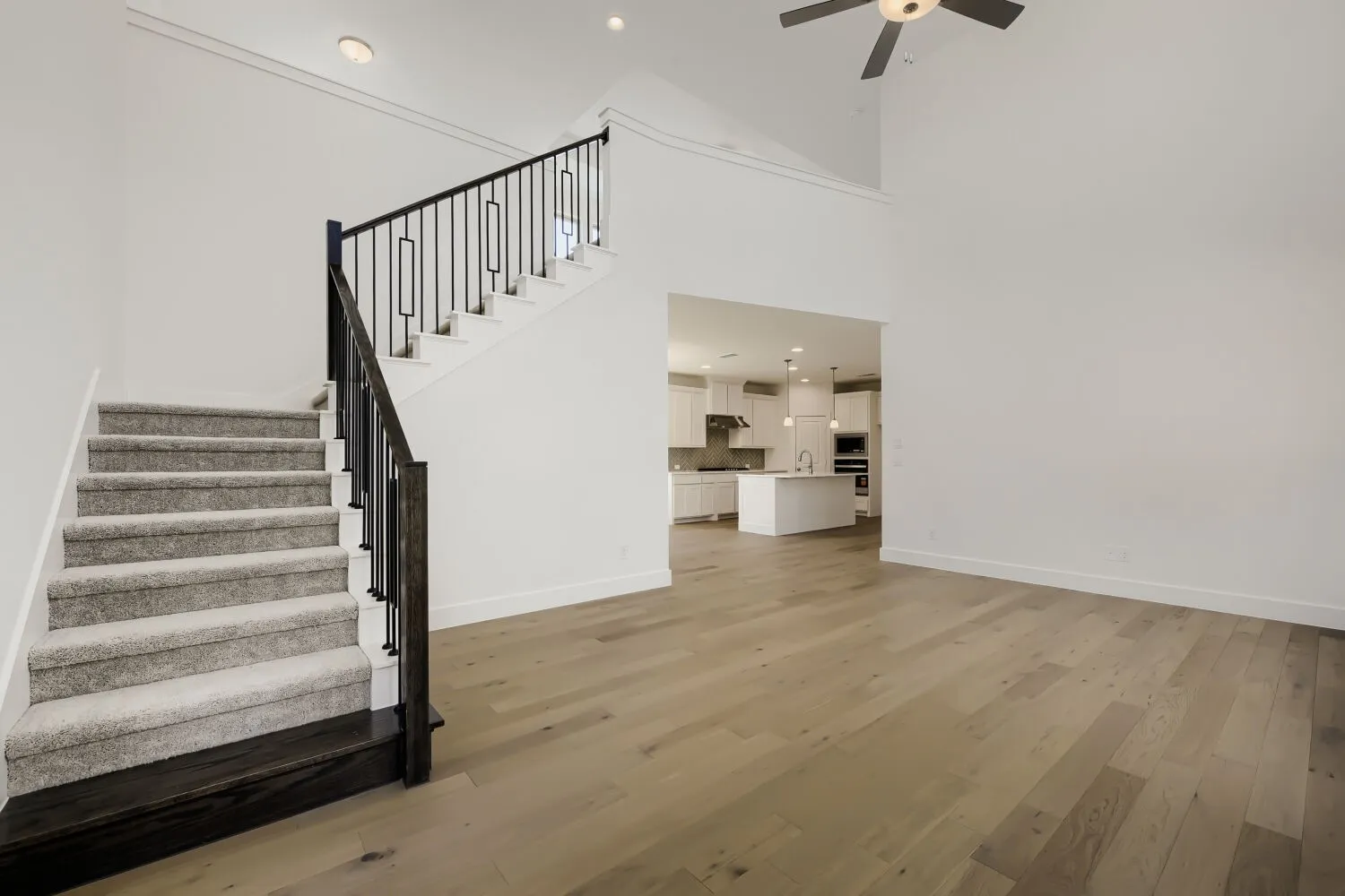 Virtually Staged Photo - Two-story living area with high ceilings, dark wood-finish flooring, and a staircase with black metal balusters
