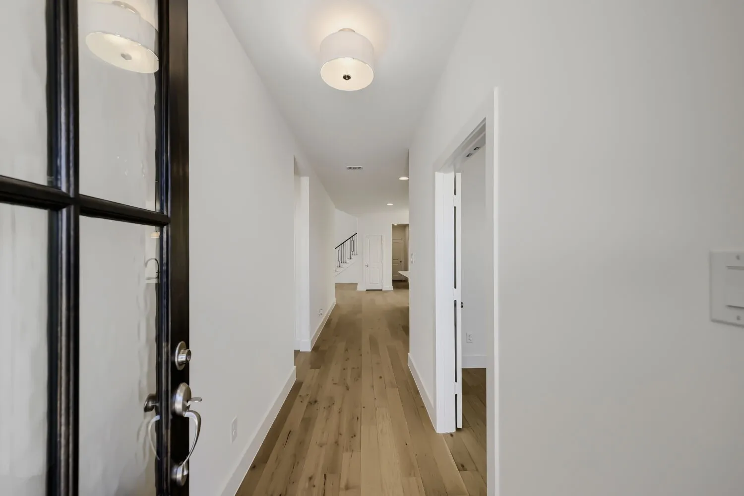 Entryway featuring wood-finish flooring, white walls, a black-framed glass entry door with silver hardware, and a ceiling-mounted light fixture