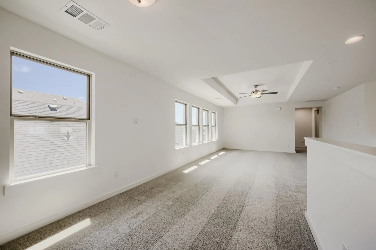 Bright upper-level space featuring multiple windows, recessed lighting, a tray ceiling, a ceiling fan with integrated lighting, and carpet flooring
