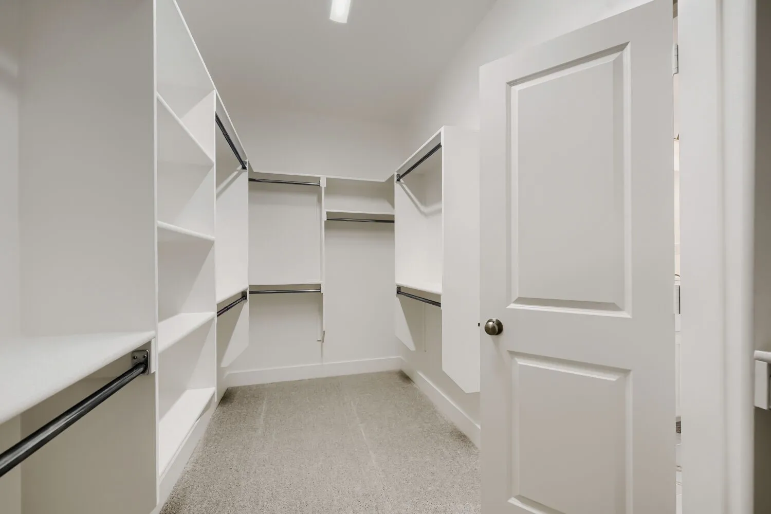 Walk-in closet featuring built-in shelving, multiple hanging rods, and light gray carpeting